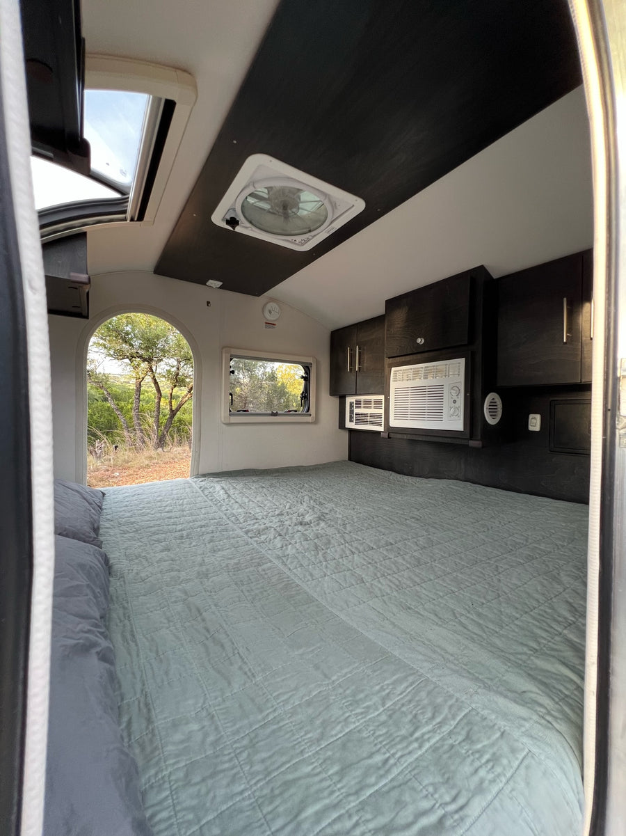 Inside a comfy RV rental bedroom featuring a spacious bed, AC units, and scenic outdoor views.