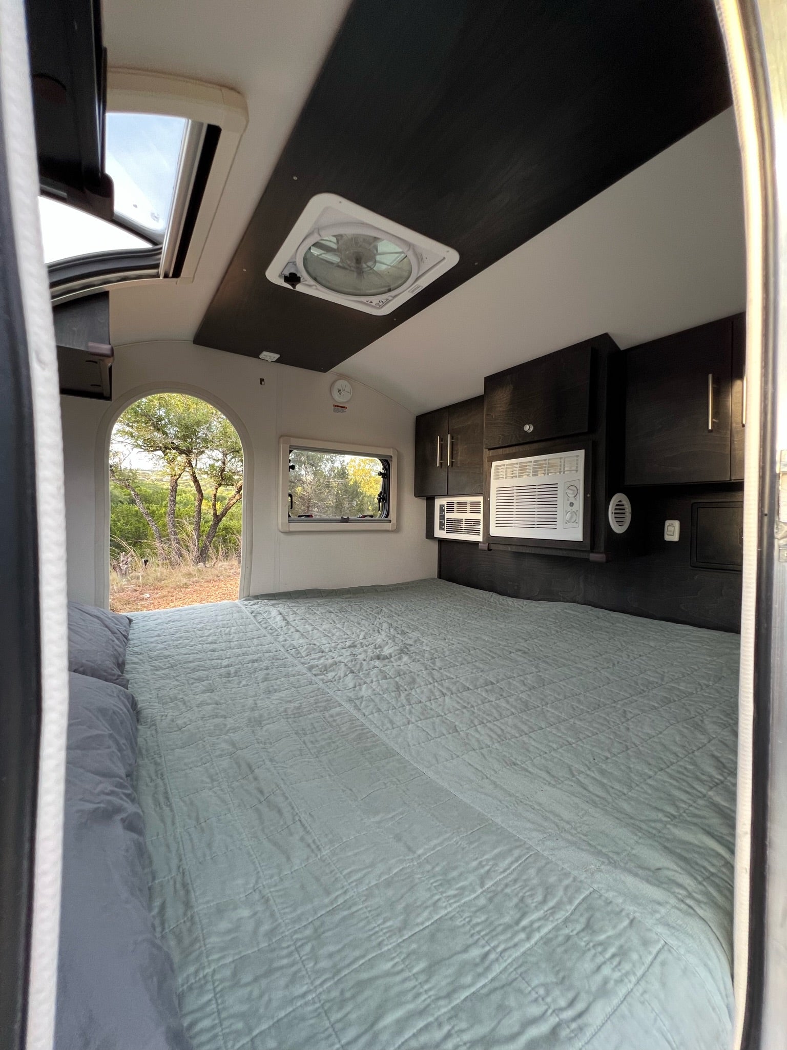 Inside a comfy RV rental bedroom featuring a spacious bed, AC units, and scenic outdoor views.