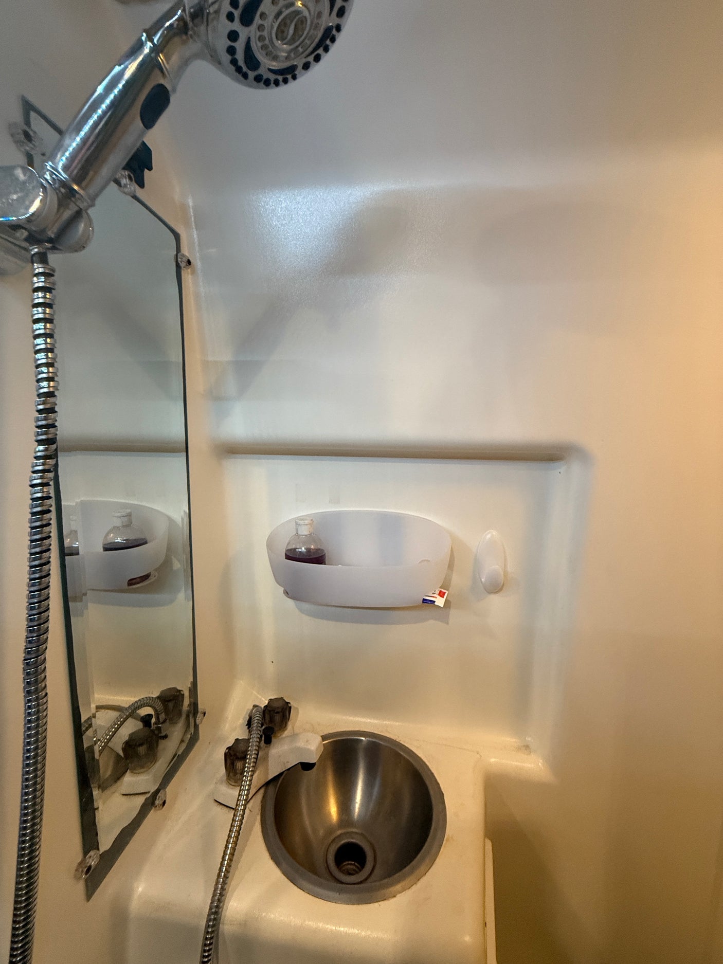 RV rental compact wet bath: chrome shower, stainless steel sink, mirror, and toiletries caddy.