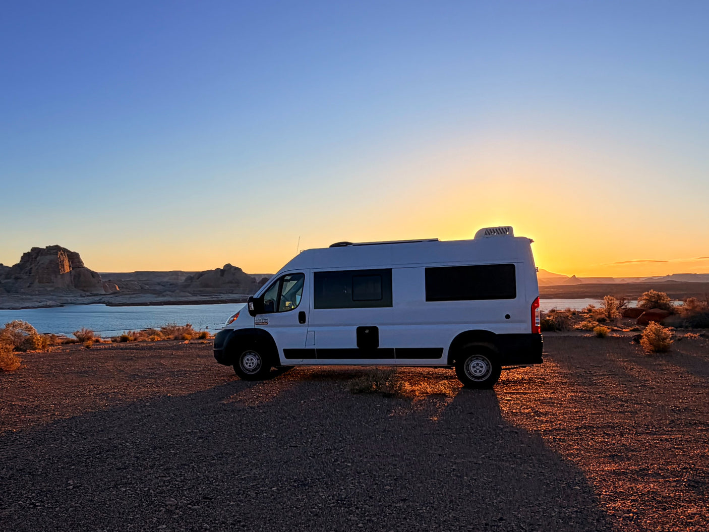 RV rental parked at sunset by a lake, with rocky formations and a golden sky. Perfect for a scenic road trip.
