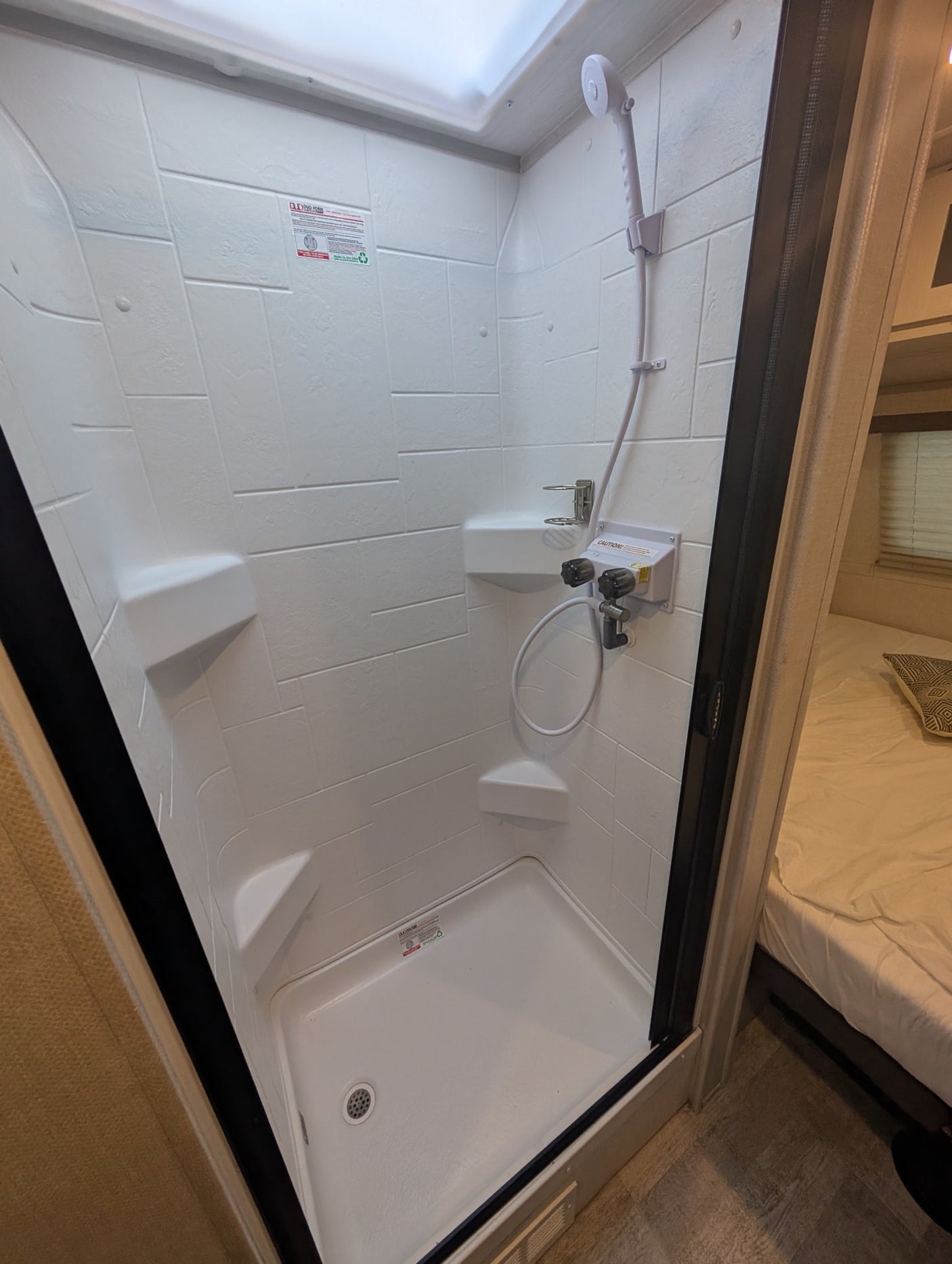 Inside an RV rental: a compact white shower with a handheld showerhead, controls, and shelf, designed for travel convenience.