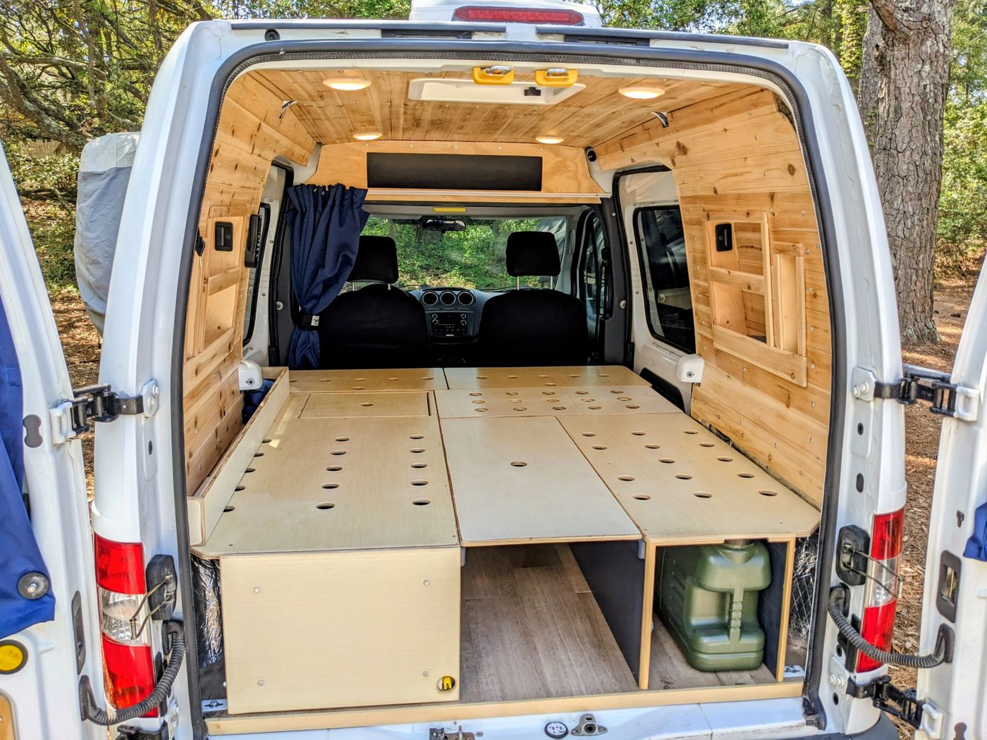 Inside a custom rv rental van, featuring wood paneling, a modular bed platform, under-bed storage, and overhead lights.