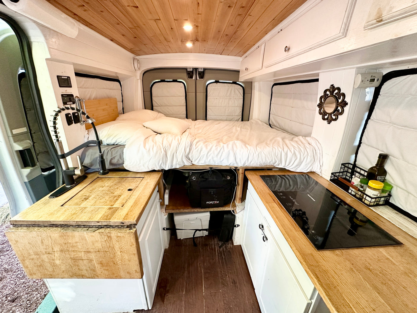 RV rental van's cozy interior: kitchen with faucet, induction cooktop, and comfortable bed for compact van life living.