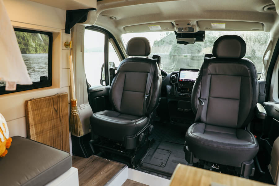 RV rental: Camper van interior with front seats, dash, and lake views. A broom hangs near a side window.