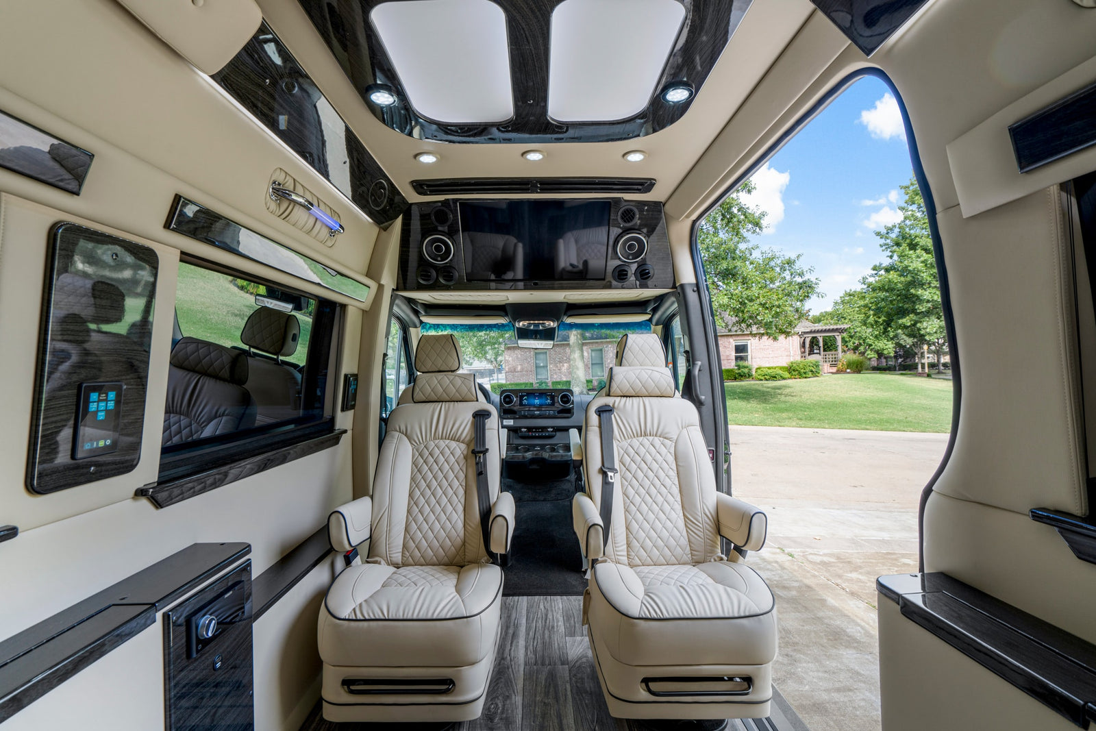 Spacious, luxury RV rental interior with cream leather seats, sleek wood finishes, and a bright view of a house and yard.