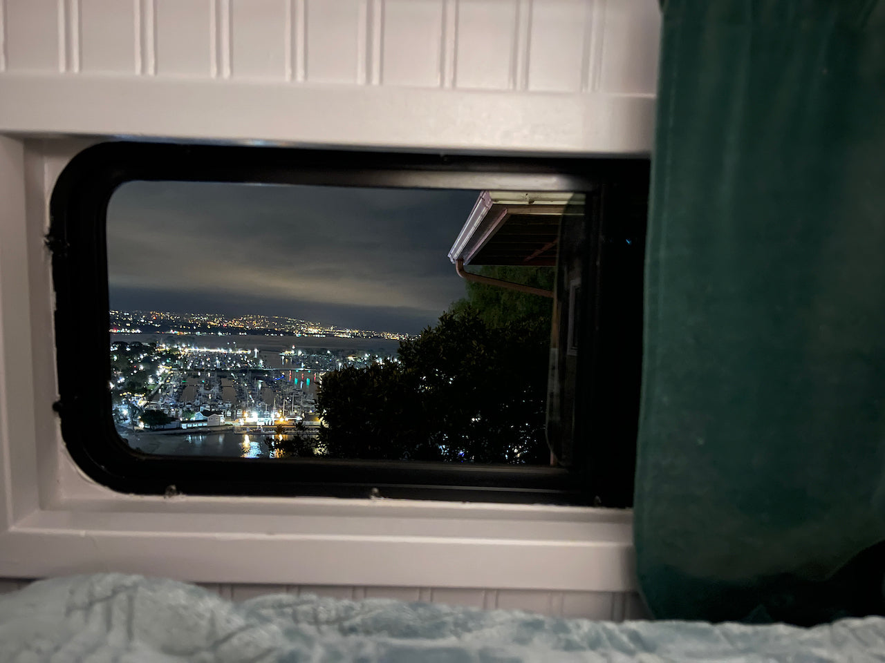 Stunning night view from an RV rental window, showing a bustling marina and city lights across the water at night.
