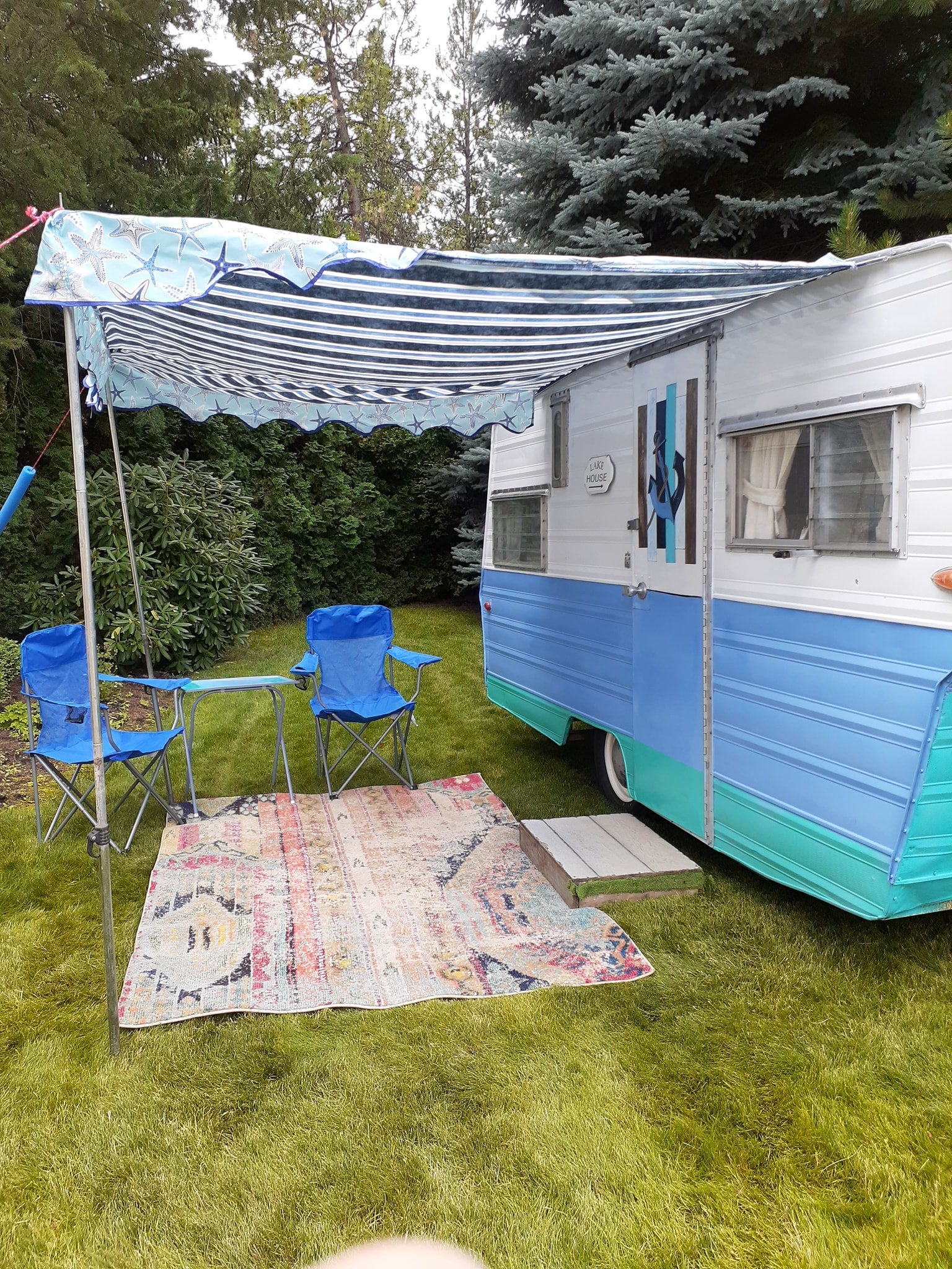 This inviting rv rental offers a comfortable outdoor setup with a striped awning, colorful rug, and blue chairs on green grass.