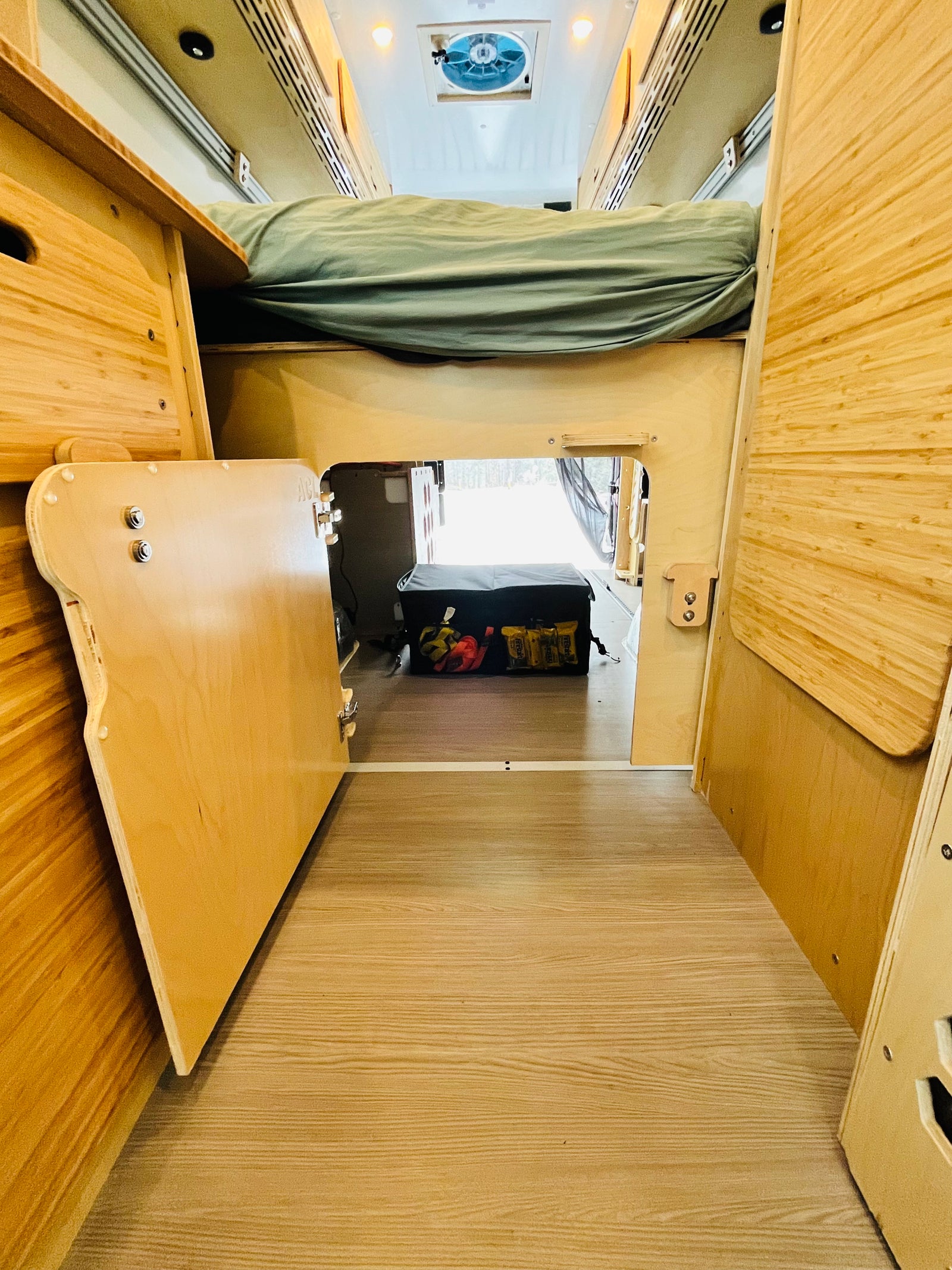 Cozy RV rental interior featuring an overhead bed, under-bed storage with a cooler, and light wood paneling.