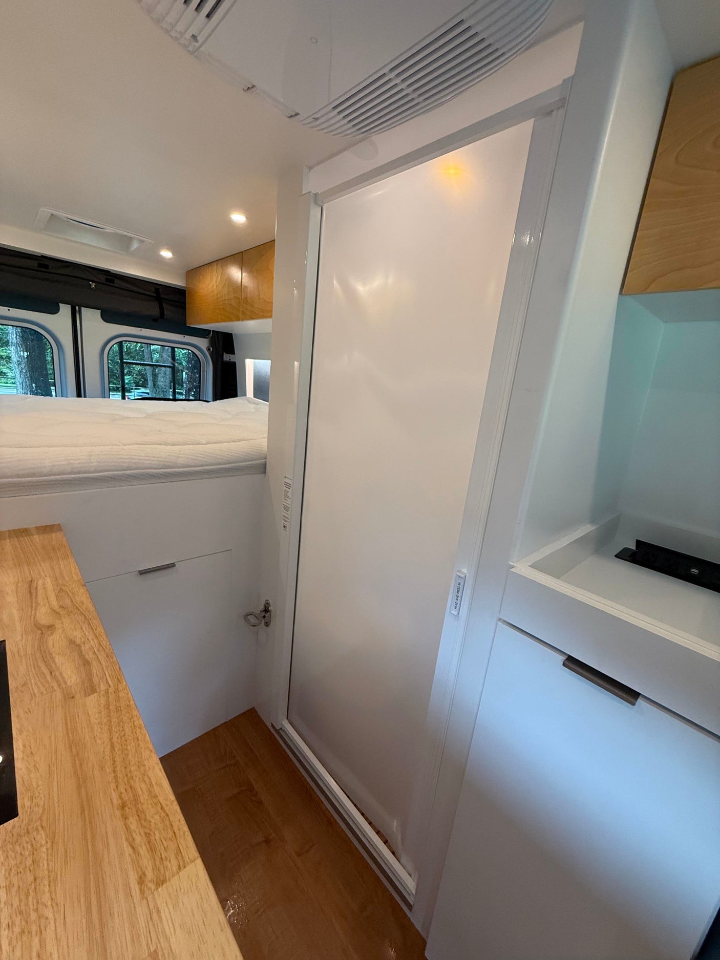 Explore this RV rental's modern interior: raised bed, wood kitchen counter, and sleek white bathroom/shower door.