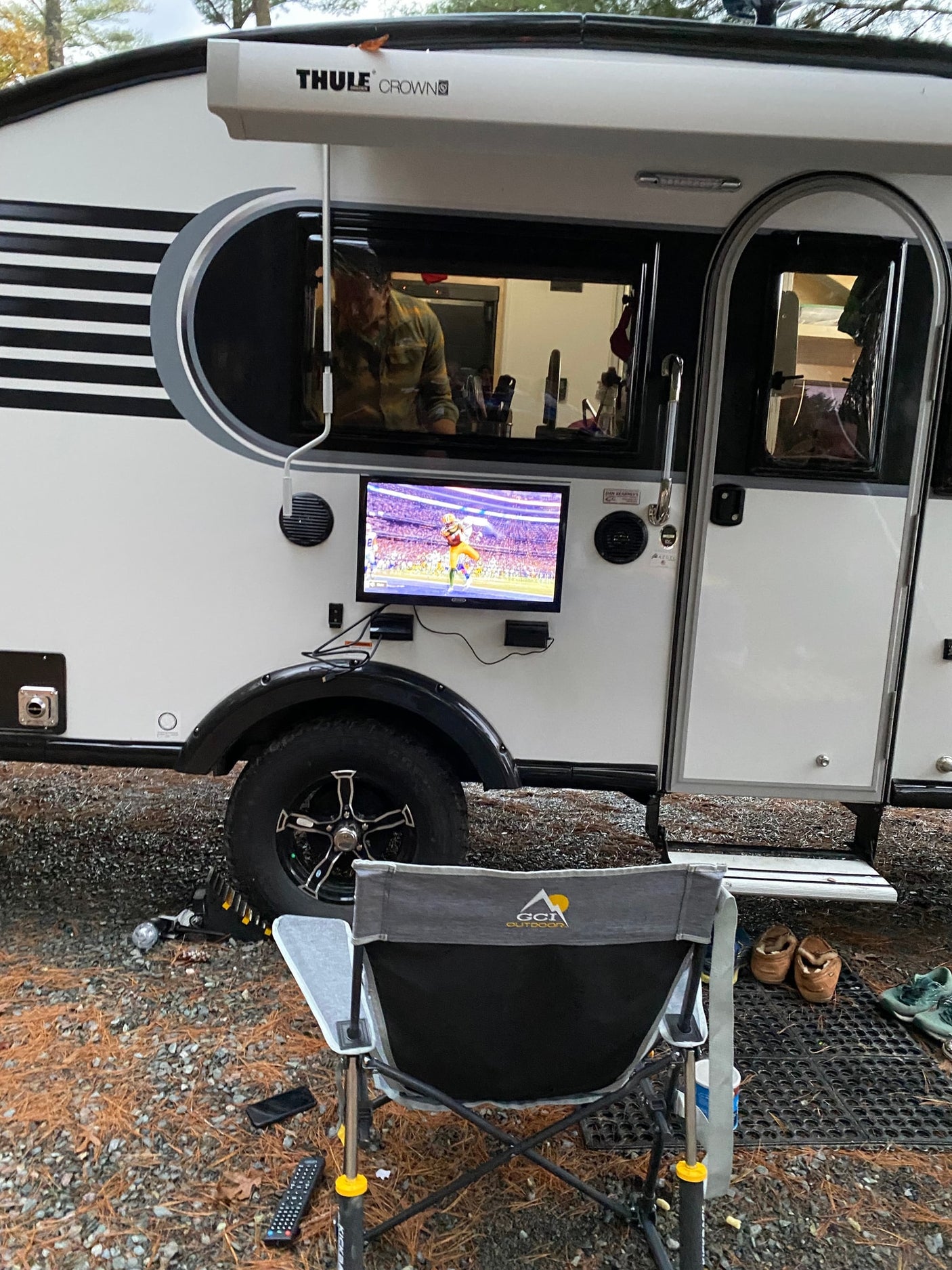 An RV rental with an outdoor TV showing a football game. A chair and remote invite camping leisure.