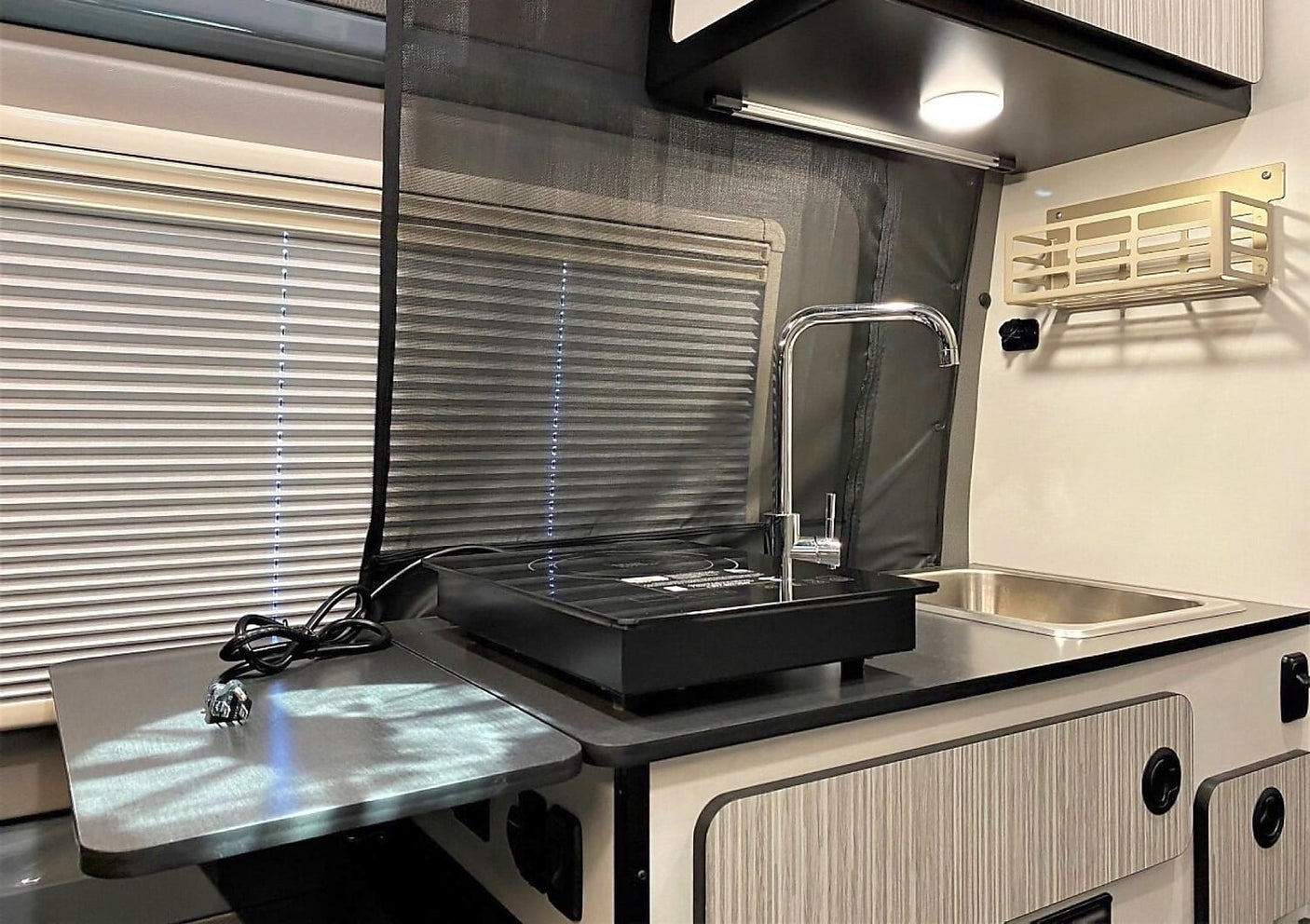 RV rental kitchen: Compact design with sink, induction cooktop, folding counter, and dual window blinds.