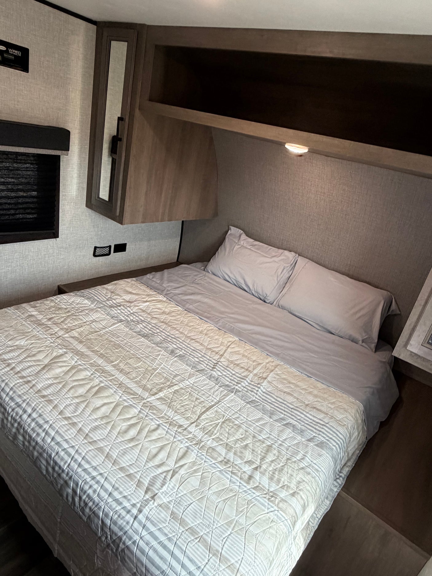 Cozy RV rental bedroom with a striped and quilted bed, overhead storage, and bedside charging, perfect for comfortable journeys.