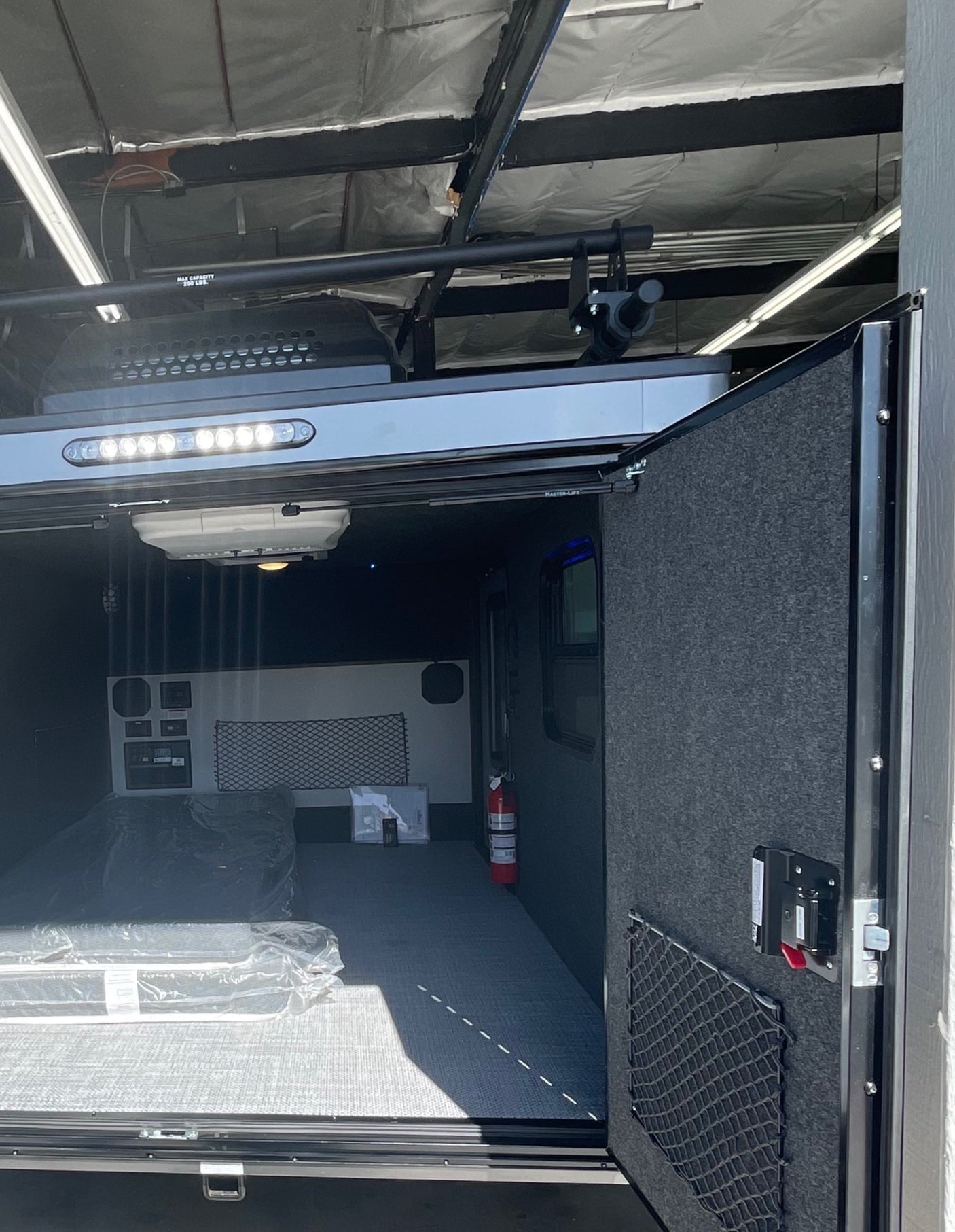 RV rental toy hauler interior: spacious cargo area with ramp door, overhead lighting, control panels, and mattress for versatile use.