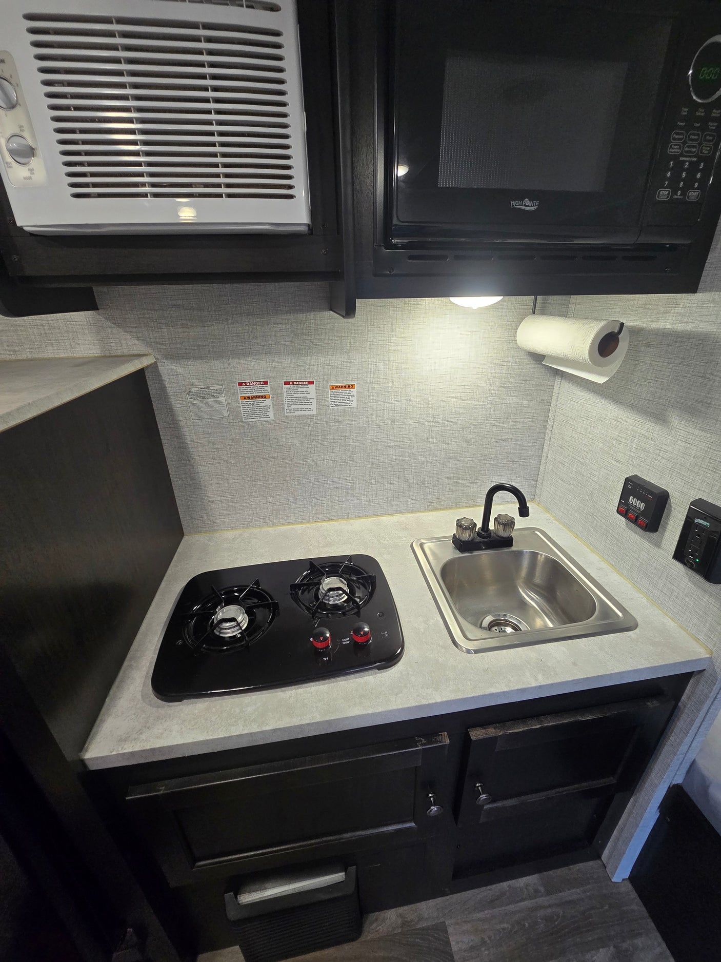 Compact RV rental kitchen featuring a microwave, two-burner stovetop, and sink, designed for efficient use of space.