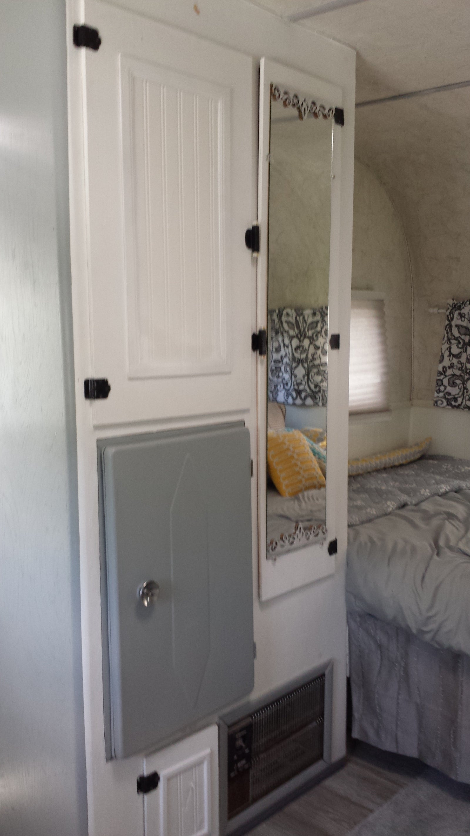 Inside a cozy RV rental: white storage cabinet, integrated mirror showing the bed, and a lower utility panel for convenience.