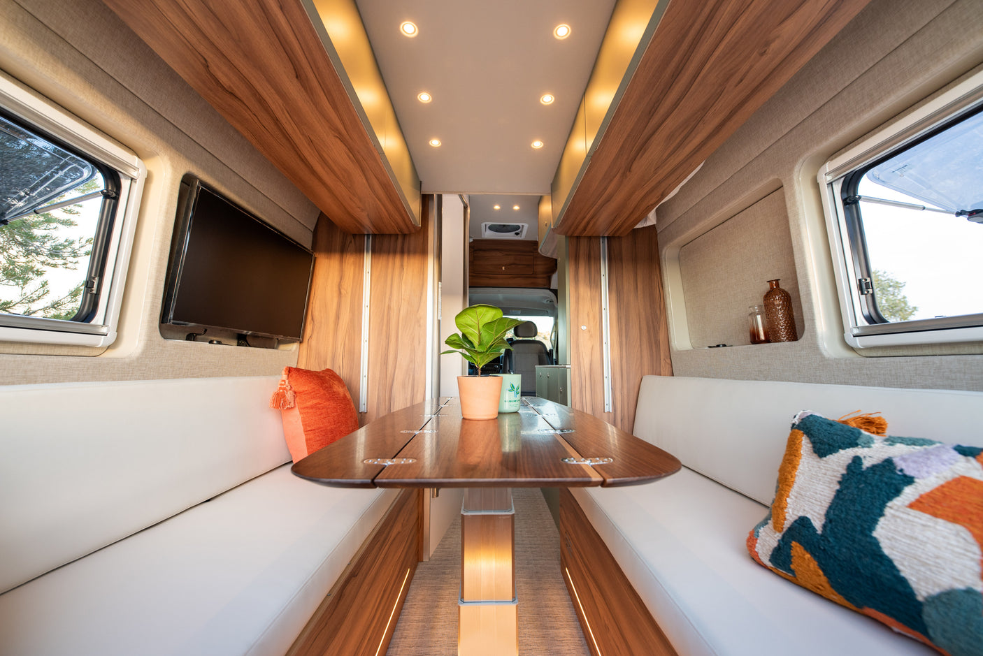 Inside a stylish RV rental: a bright dining space with comfortable white seating, a wood table, and ambient lighting.