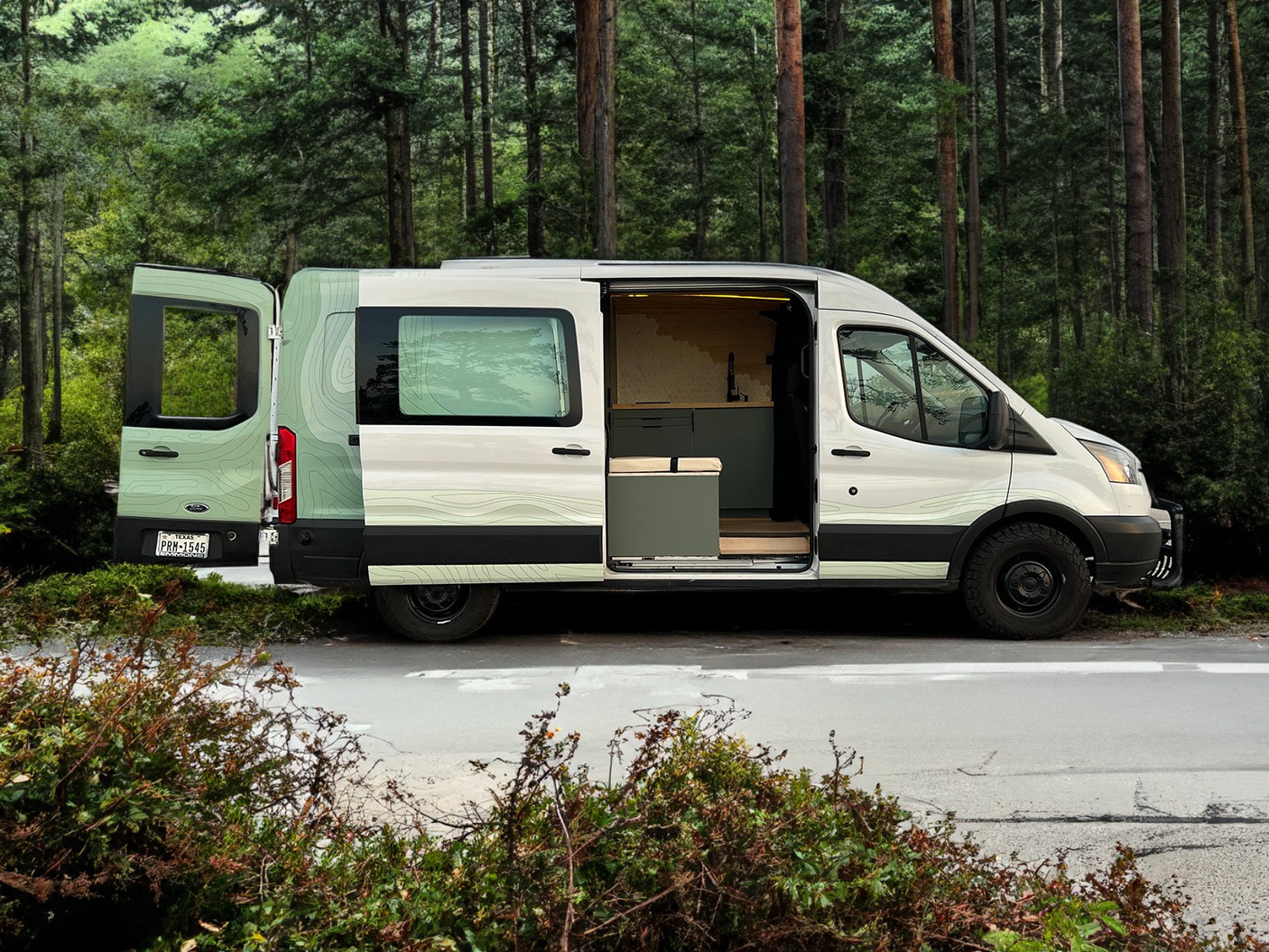 A custom Ford Transit camper van with open doors, revealing its unique interior and exterior design. Perfect for an RV rental adventure in nature.