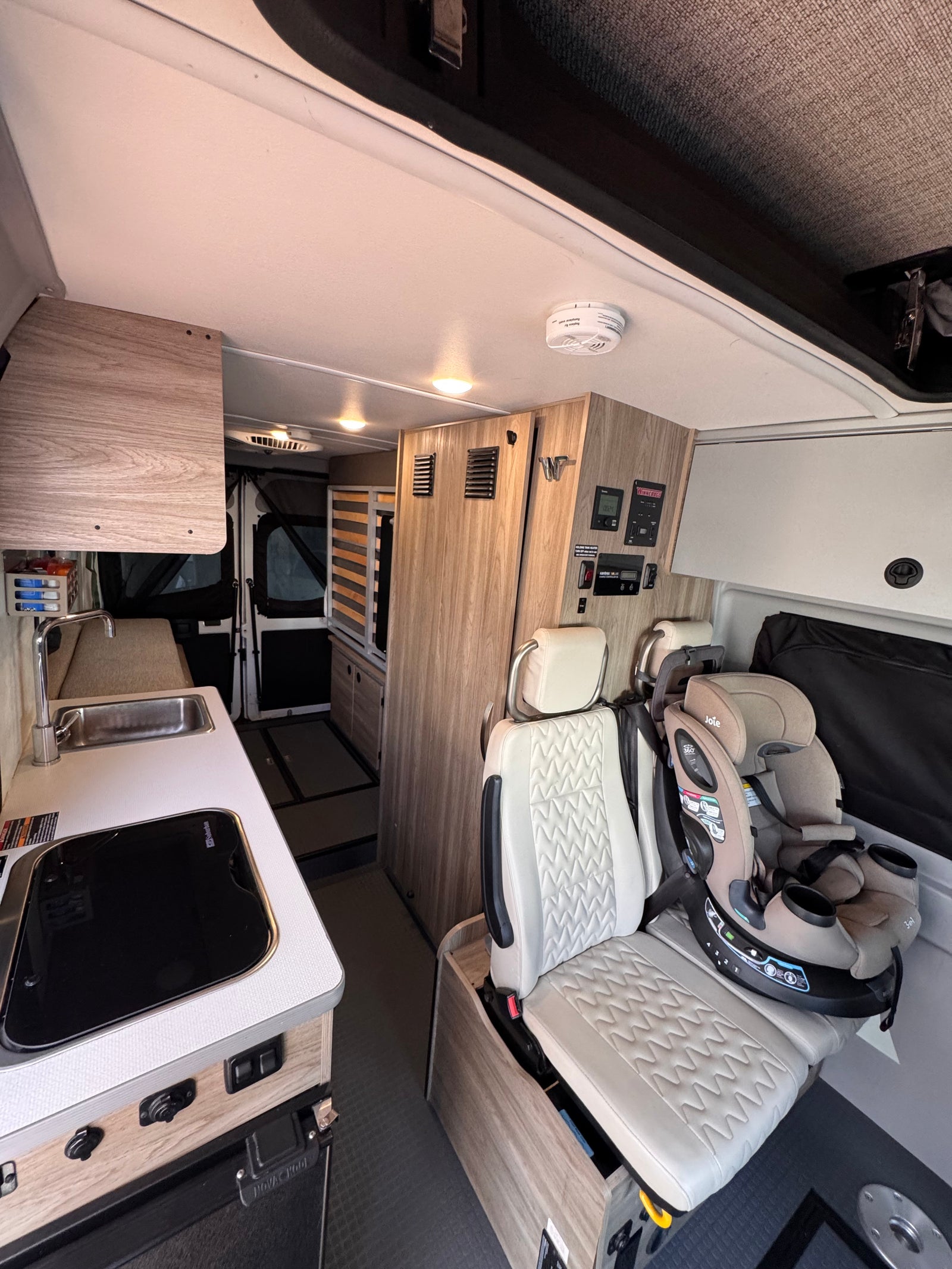 Cozy rv rental interior featuring a kitchenette, child safety seat, and pop-top roof. Ideal for family road trips.