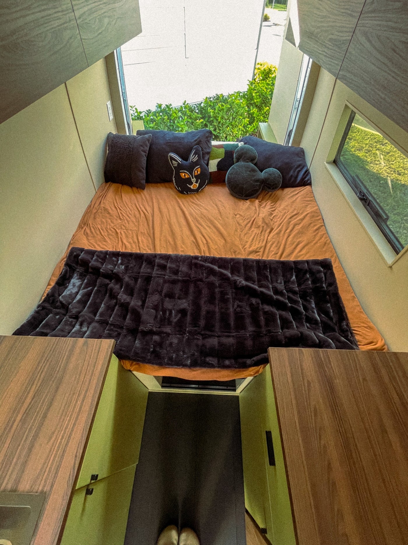 Experience a cozy rv rental! This modern sleeping nook features an orange bed, plush blanket, fun pillows, and scenic windows. — photo 6