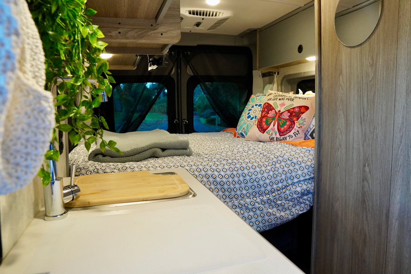 Cozy RV rental interior featuring a comfortable bed, a compact kitchen with sink, and scenic rear window views.