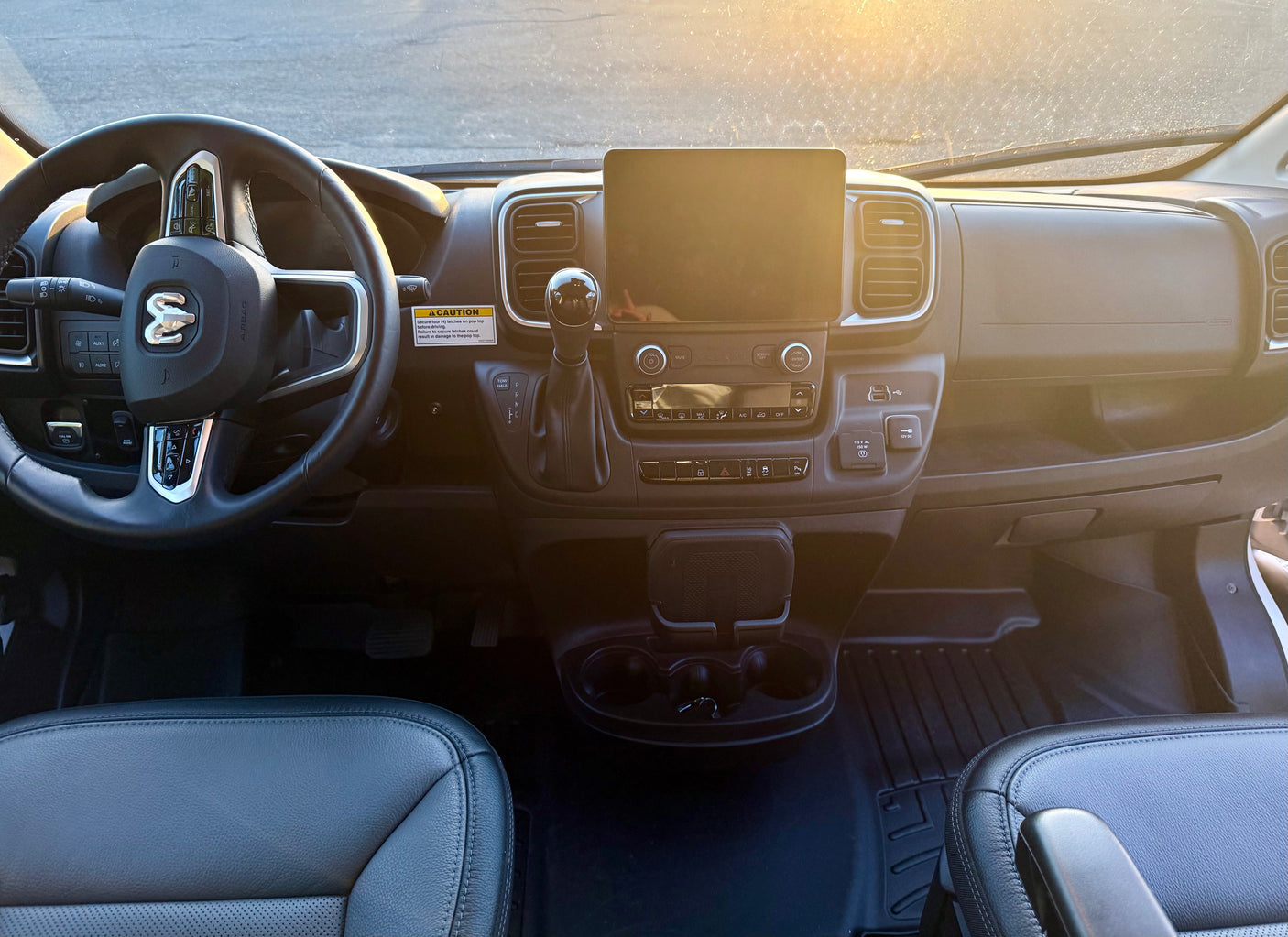 Dashboard and cockpit of a clean RV rental, viewed from the driver's seat, showing the steering wheel, infotainment, and controls.