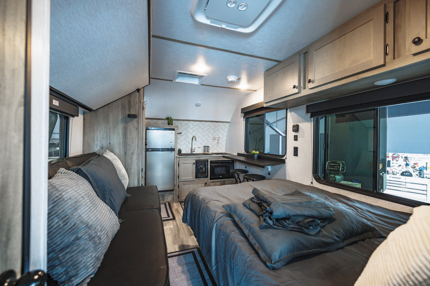 RV rental interior showcasing a comfortable bed, sofa with pillows, and a modern kitchen area, designed for cozy travel adventures.