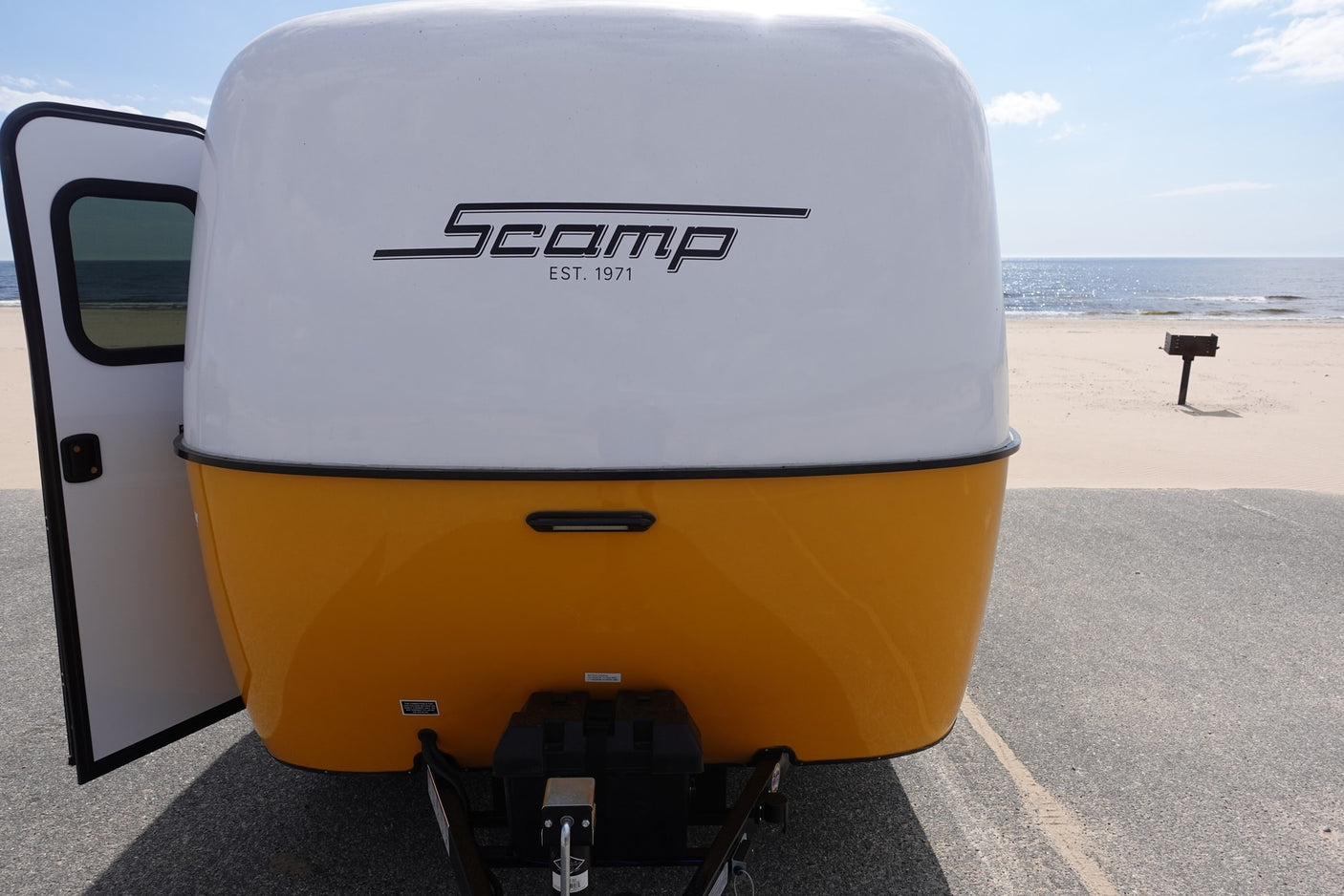 Scamp travel trailer RV rental at the beach, its open door revealing an ocean view. Perfect for adventure.