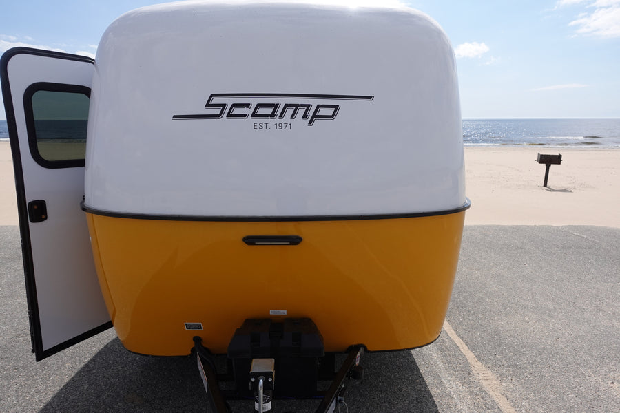 Scamp travel trailer RV rental at the beach, its open door revealing an ocean view. Perfect for adventure.