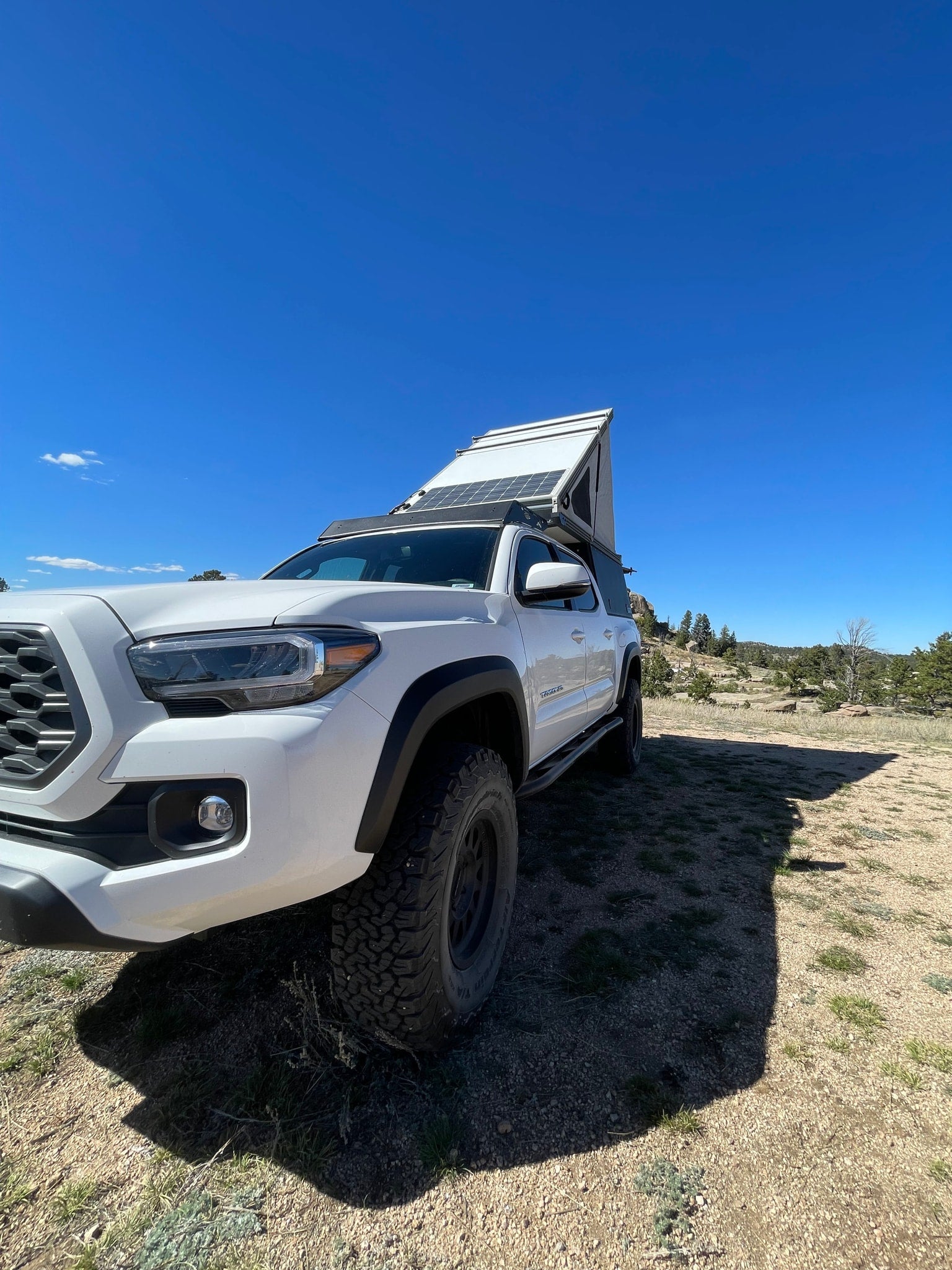 White Tacoma truck with pop-up camper & solar panels, ready for RV rental overlanding adventure.