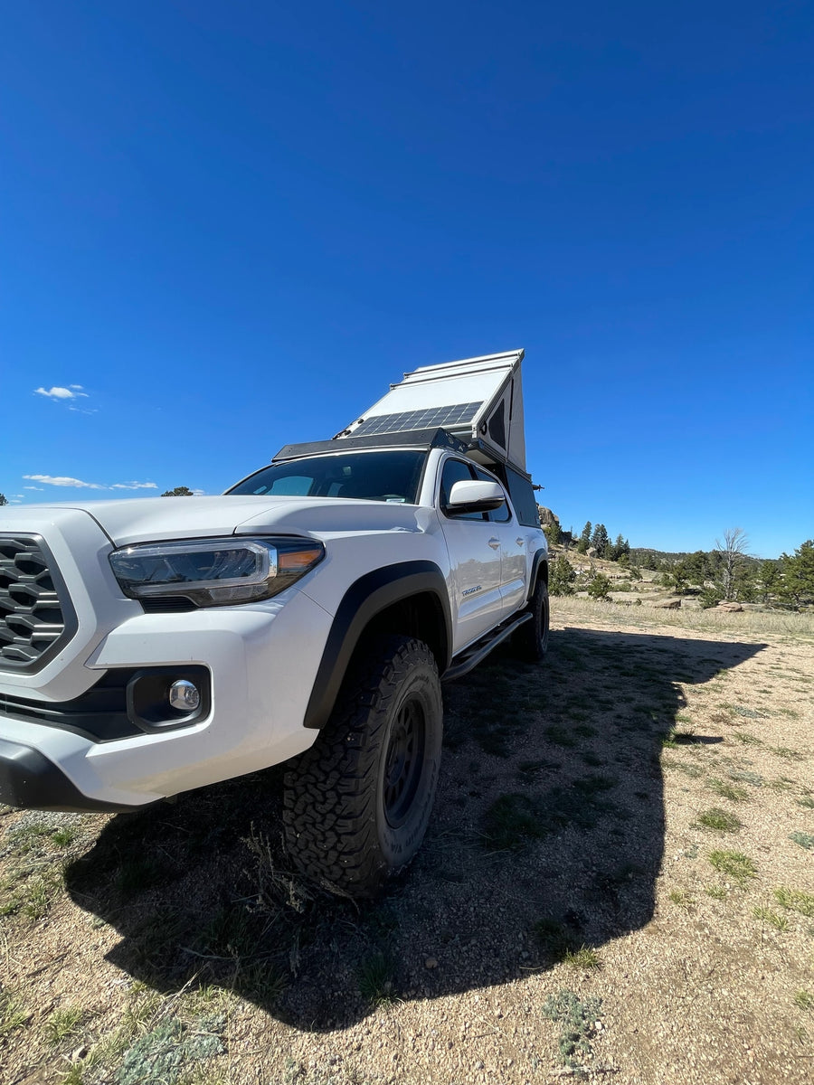 White Tacoma truck with pop-up camper & solar panels, ready for RV rental overlanding adventure.