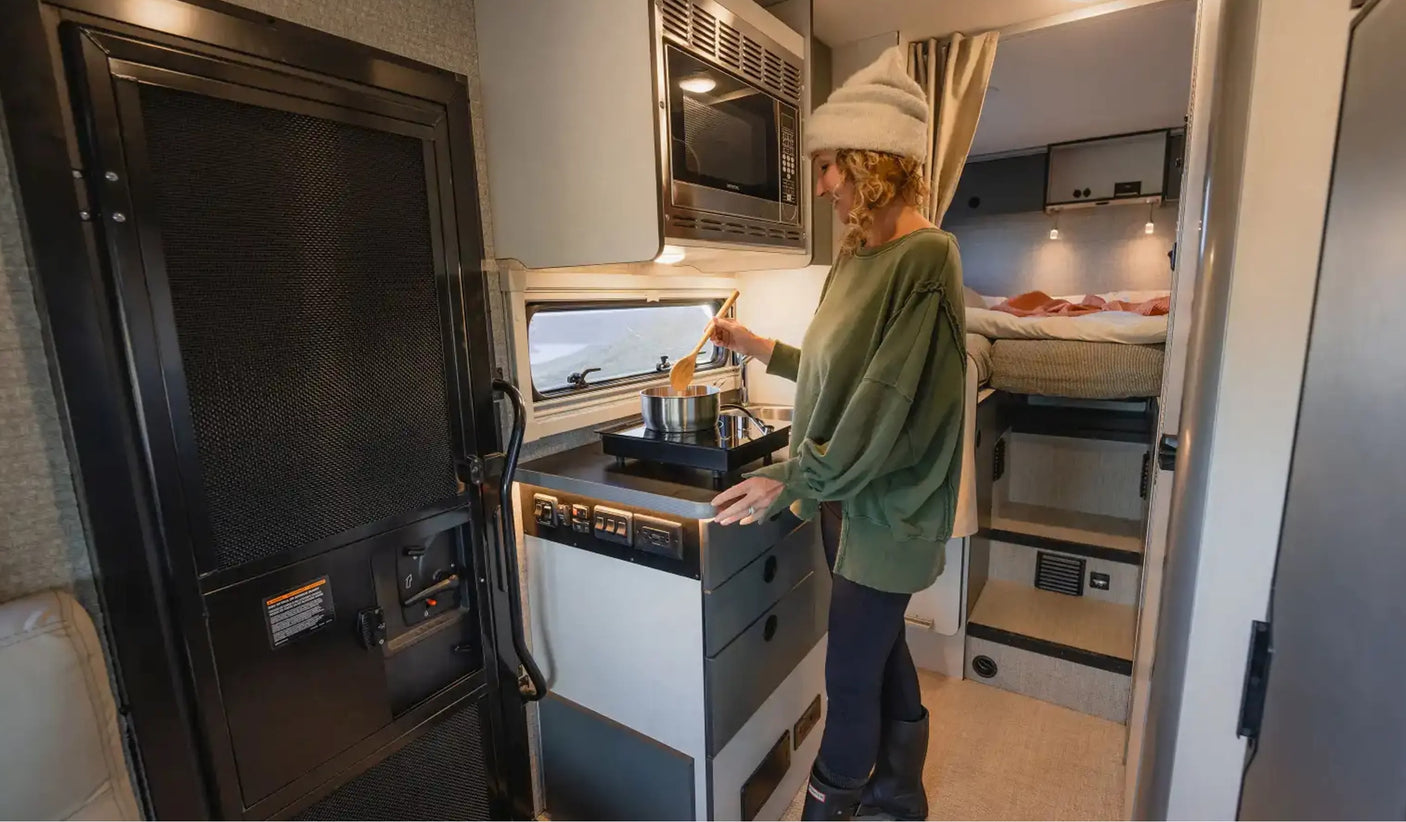 Inside an **rv rental**, a woman stirs a pot on a compact induction cooktop, highlighting functional mobile living.
