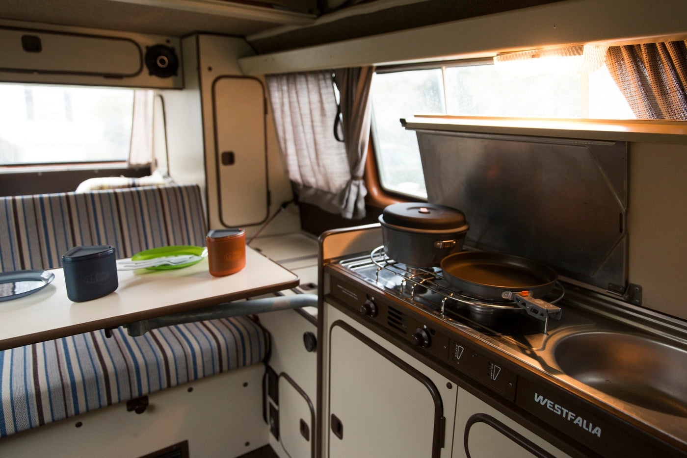 Cozy Westfalia RV rental interior: compact kitchen with stove, sink, and dining area. Perfect for camping trips! — photo 5