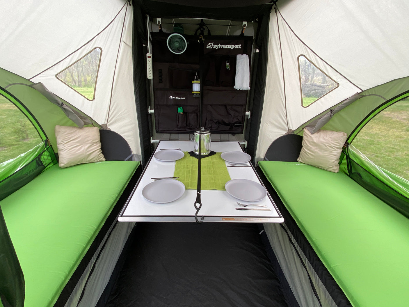 Explore this cozy RV rental interior. It features a dining table, comfortable green beds, and organized storage for your next camping trip.