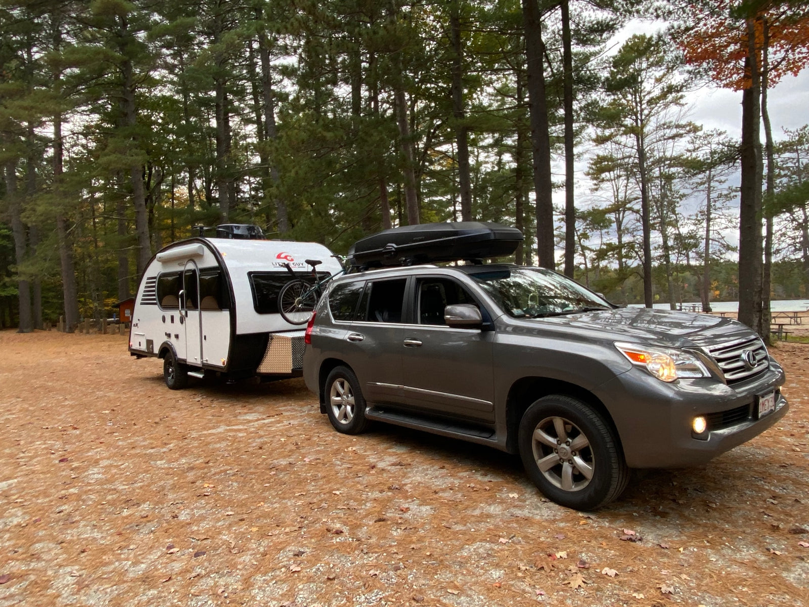 This Lexus SUV with roof cargo box tows a white Little Guy teardrop RV rental, ready for forest camping by the lake.