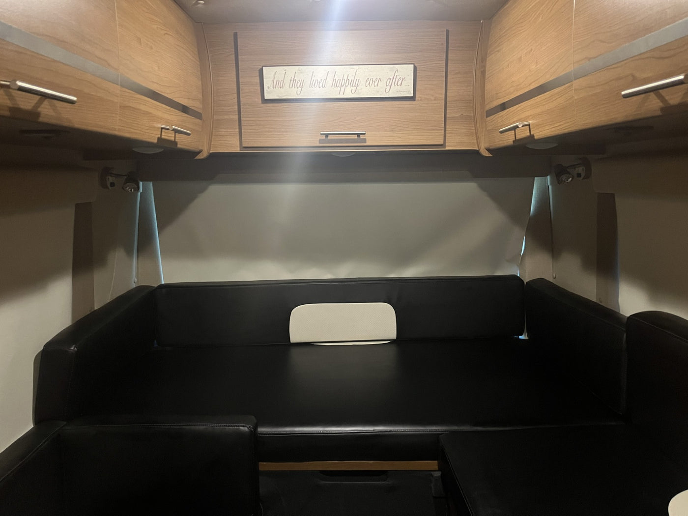Cozy RV rental interior: black convertible seating/bed, overhead wood cabinets, and 'happily ever after' sign. — photo 11