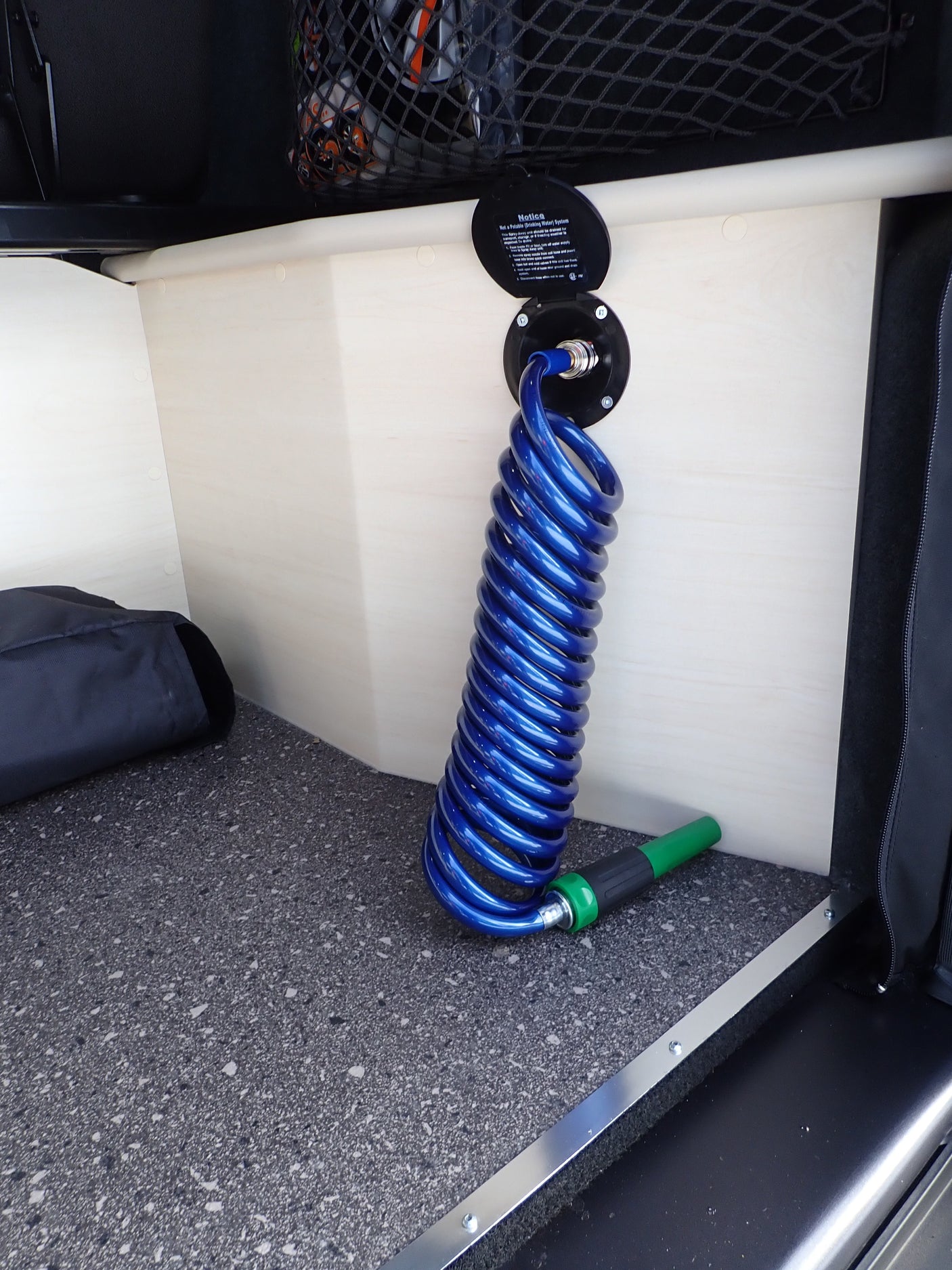 RV rental convenience: a non-potable water system with a blue coiled hose and green spray nozzle for exterior washing.