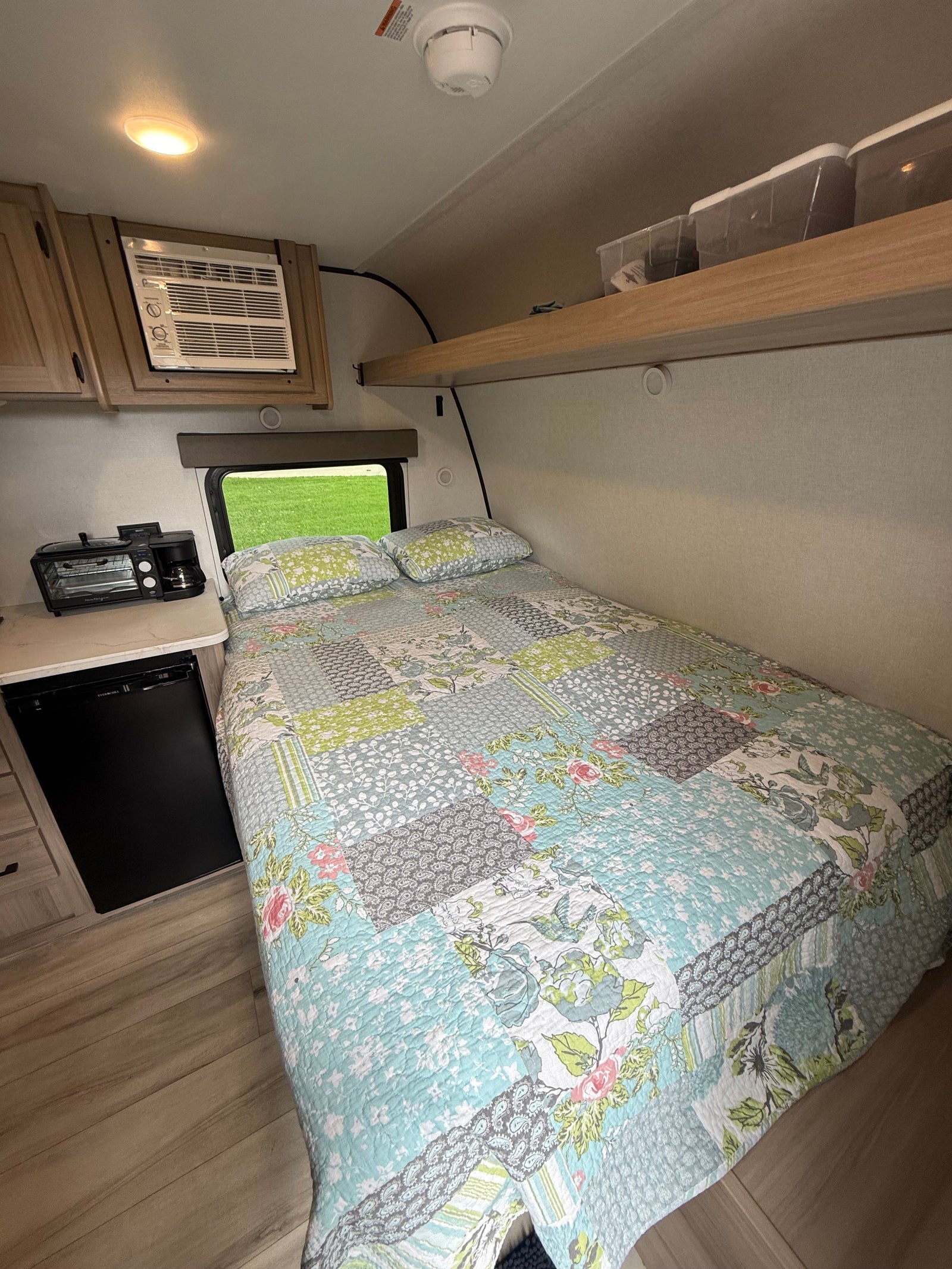 Cozy rv rental: a bedroom and kitchenette area with a colorful quilt, compact AC, mini-fridge, and toaster oven combo.