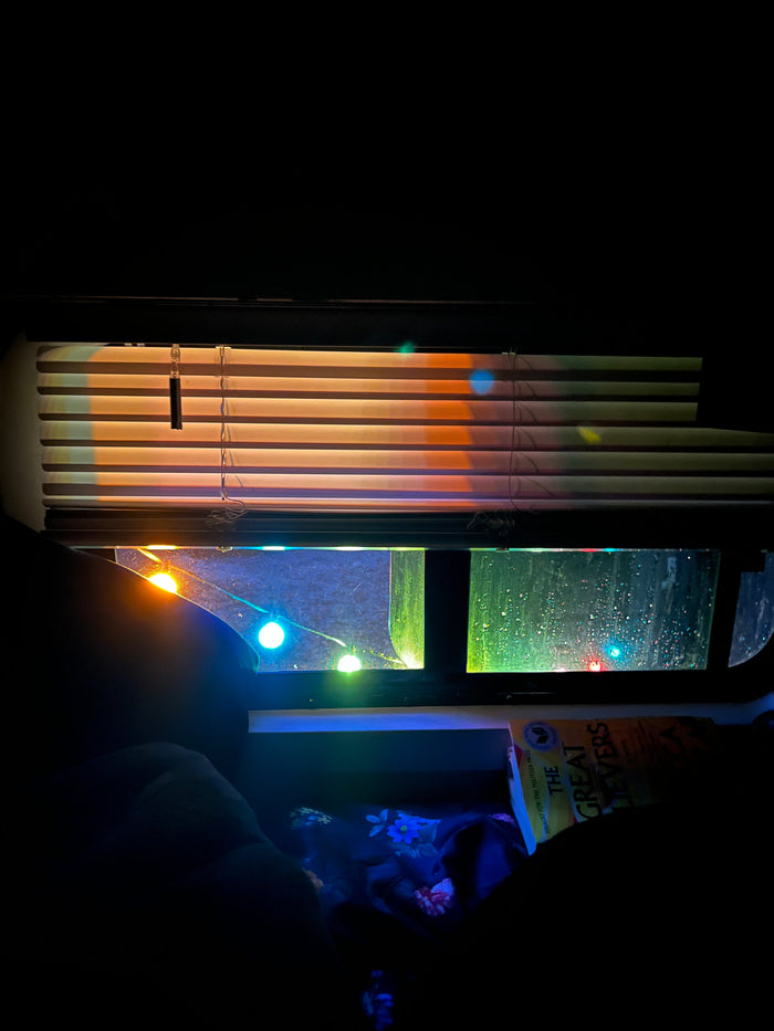 Cozy RV rental interior at night. Rain on the window, colorful string lights, and a book waiting to be read.