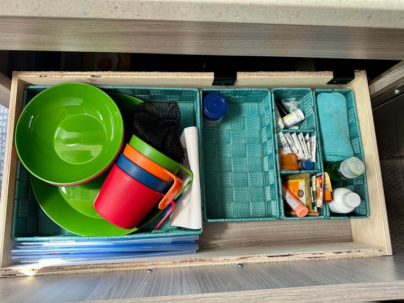 RV rental drawer featuring organized camping kitchenware: bright dishes, cups, cleaning cloths, and travel essentials in teal bins.