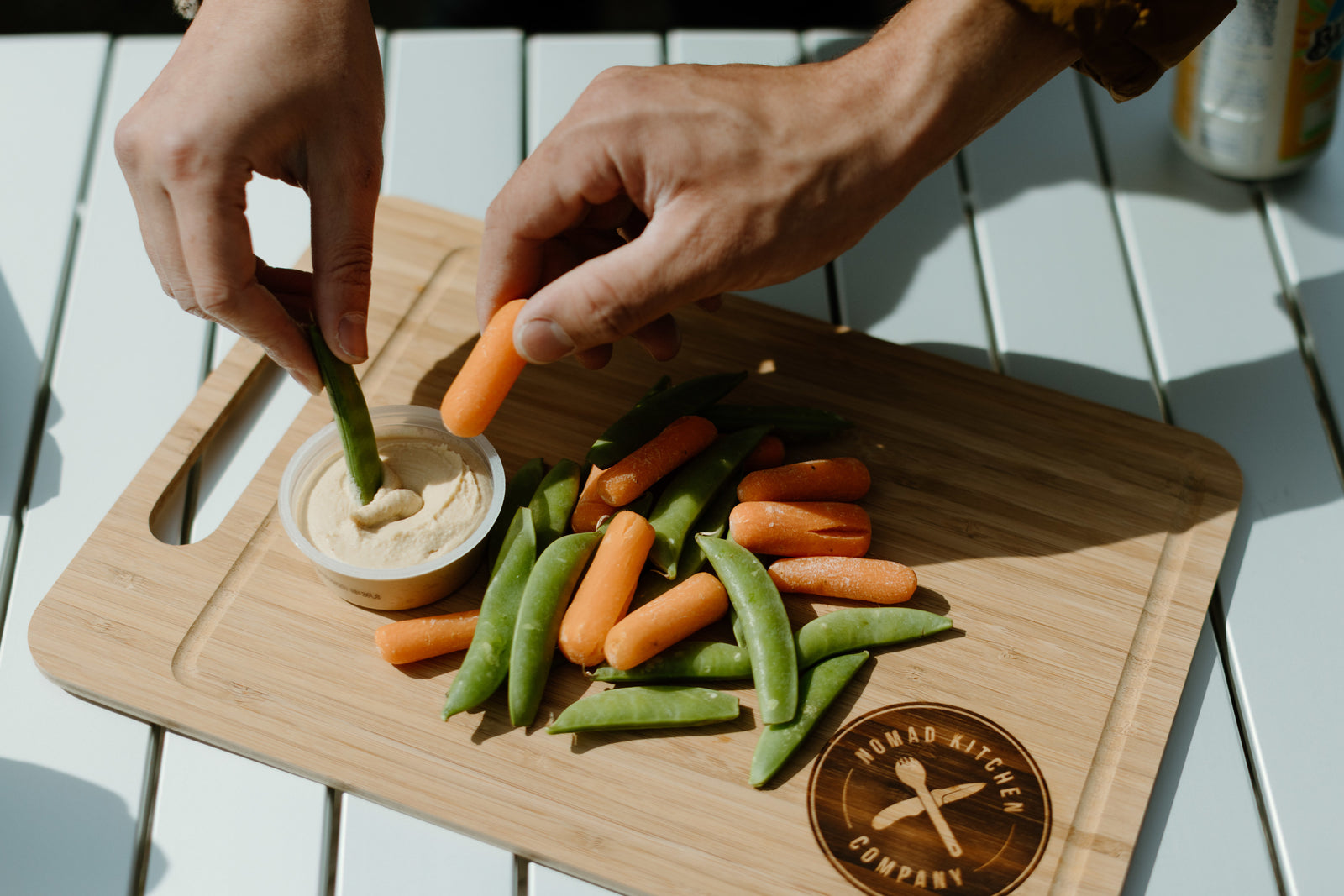Hands dip snap peas & baby carrots in hummus on a cutting board. Perfect healthy snack for an RV rental trip.