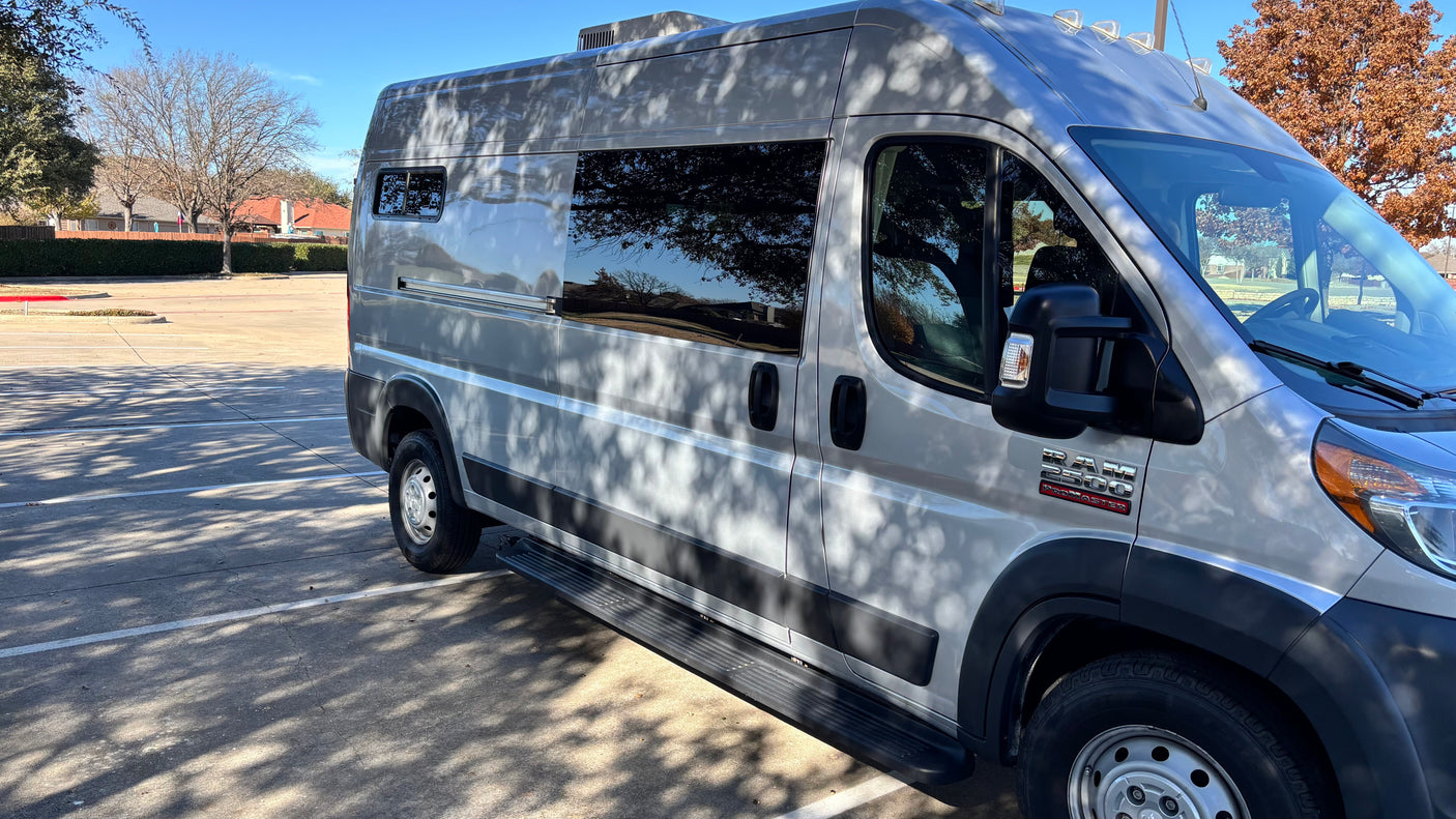 This silver Ram ProMaster van, ideal for an **rv rental**, is parked on a sunny day with tree reflections.