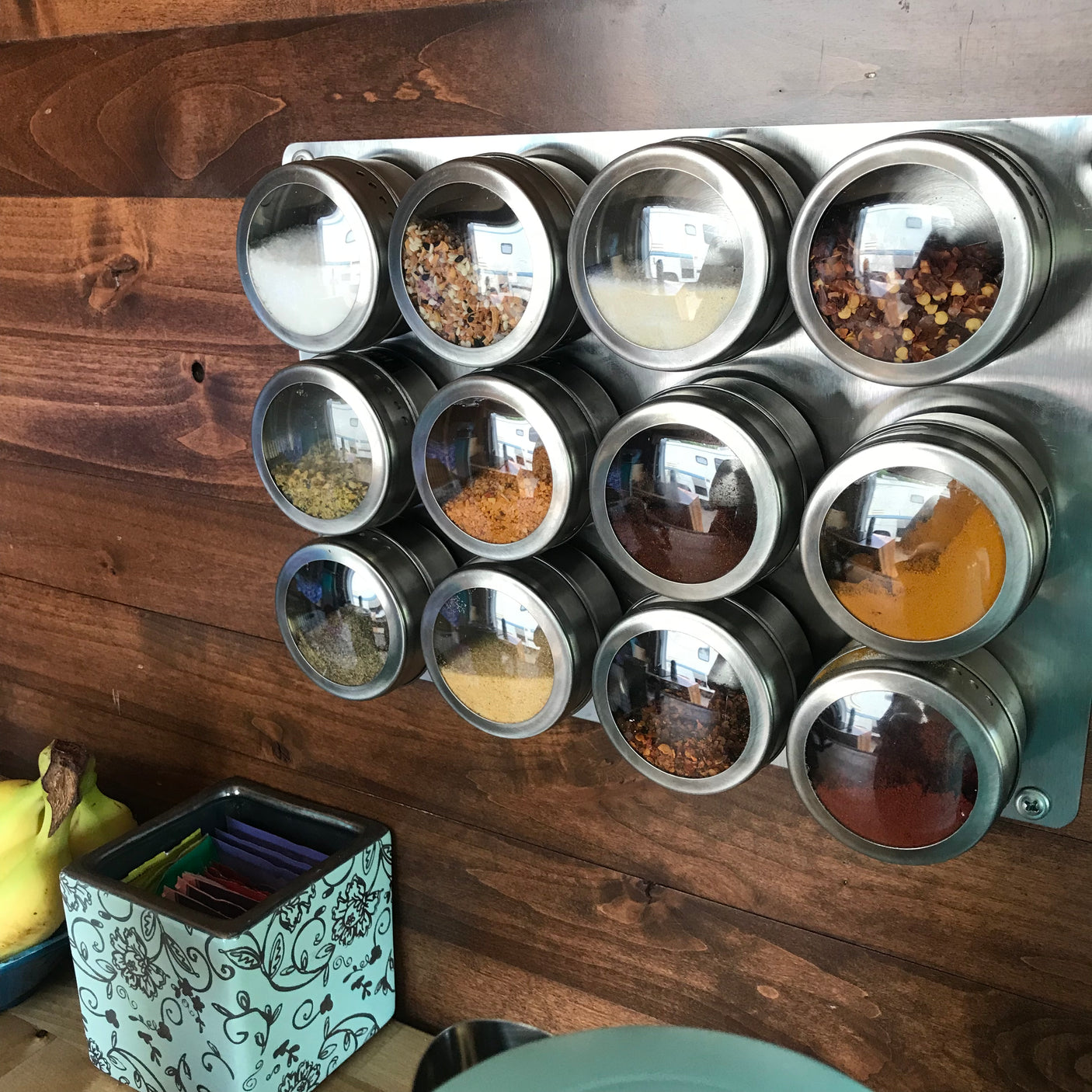 Magnetic spice rack with twelve spices on a wooden surface, reflecting an RV interior and a truck cab. Ideal for an rv rental.