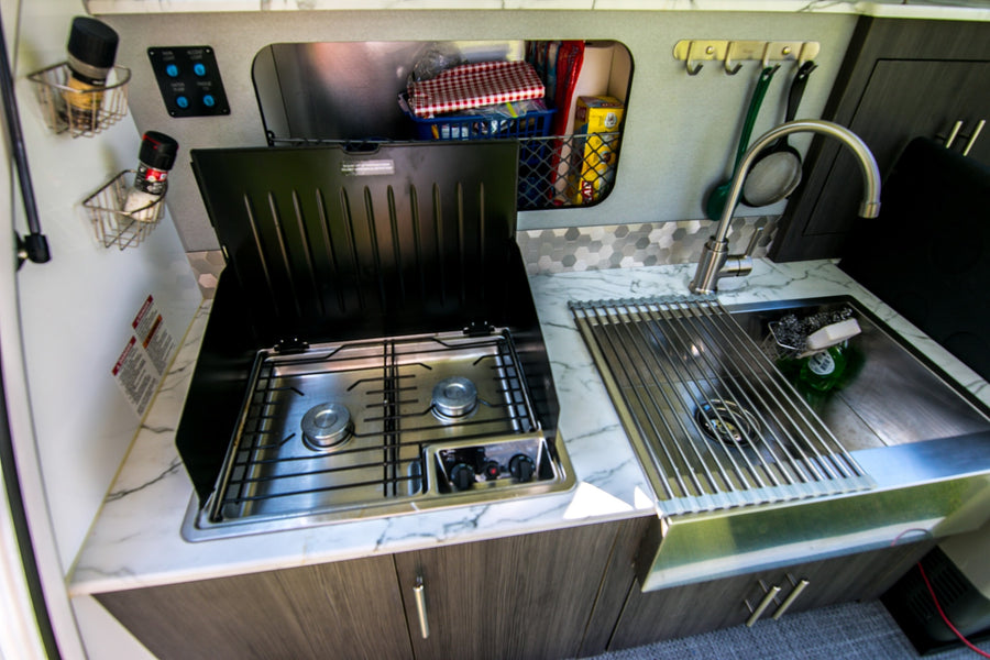 Compact rv rental kitchen: two-burner stove, sink with roll-up drying rack, and organized storage for easy meal prep on the road.