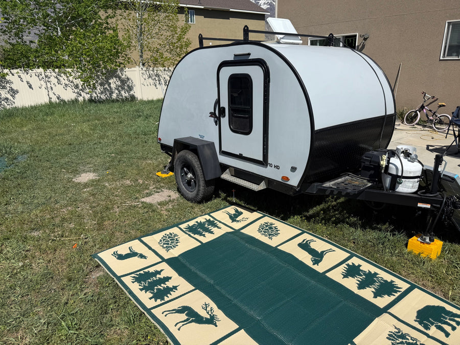 Light gray teardrop camper parked on grass with outdoor mat. Perfect for an RV rental adventure.