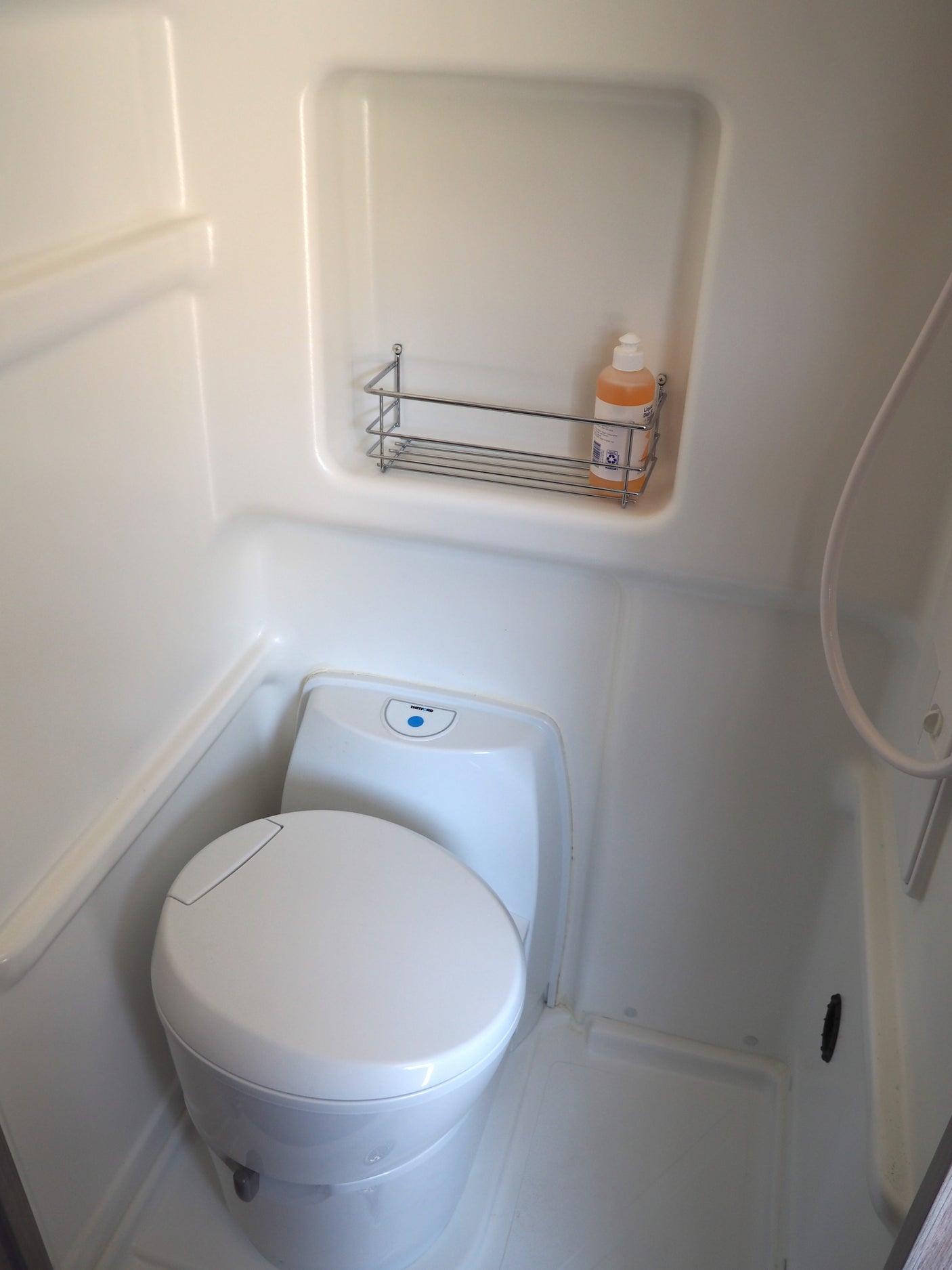 Compact RV rental wet bath with toilet, shower, and wall-mounted rack for toiletries, ideal for travel.