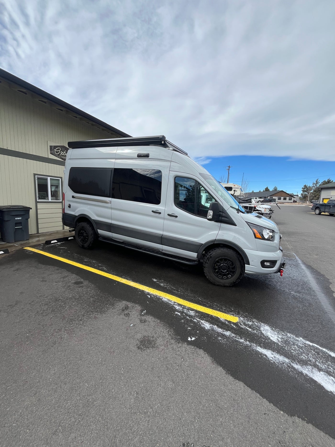 Light gray Ford Transit van (RV rental) with black wheels & roof awning, parked on an asphalt lot. — photo 5