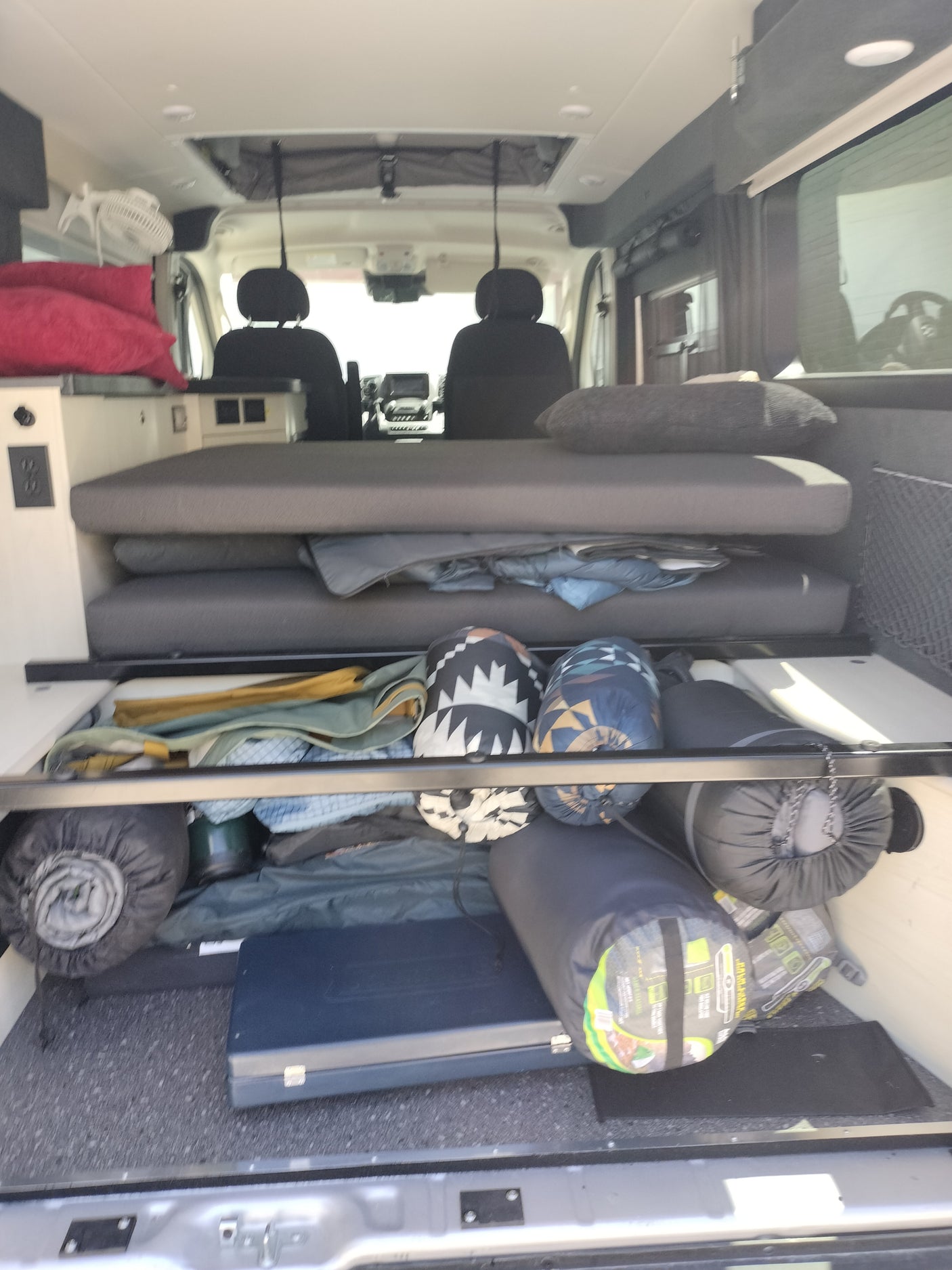 RV rental interior: A cozy camper van features a convertible bed, under-bed storage packed with gear, and visible power outlets.