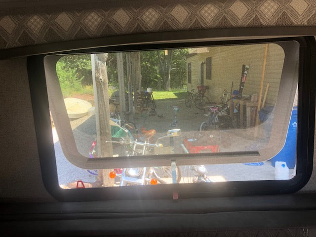 Inside RV rental: Screened window view of bikes, tools, and a house/shed on a bright day.