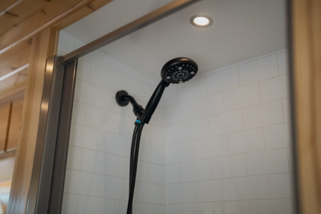 Step into comfort: This RV rental bathroom features a modern black shower head, white tiled walls, and a bright ceiling light.