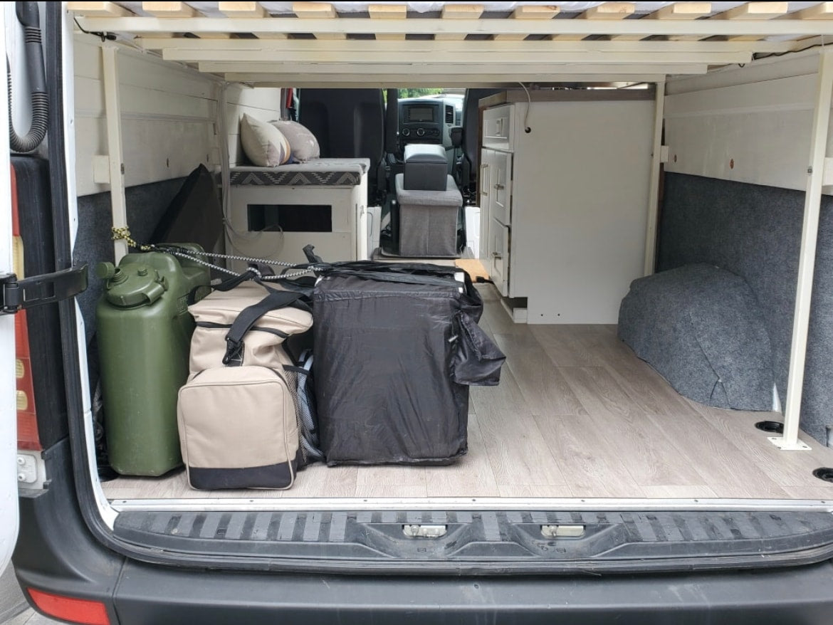 RV rental: Camper van interior features elevated bed, under-bed storage, a water can, and built-in cabinet. — photo 12